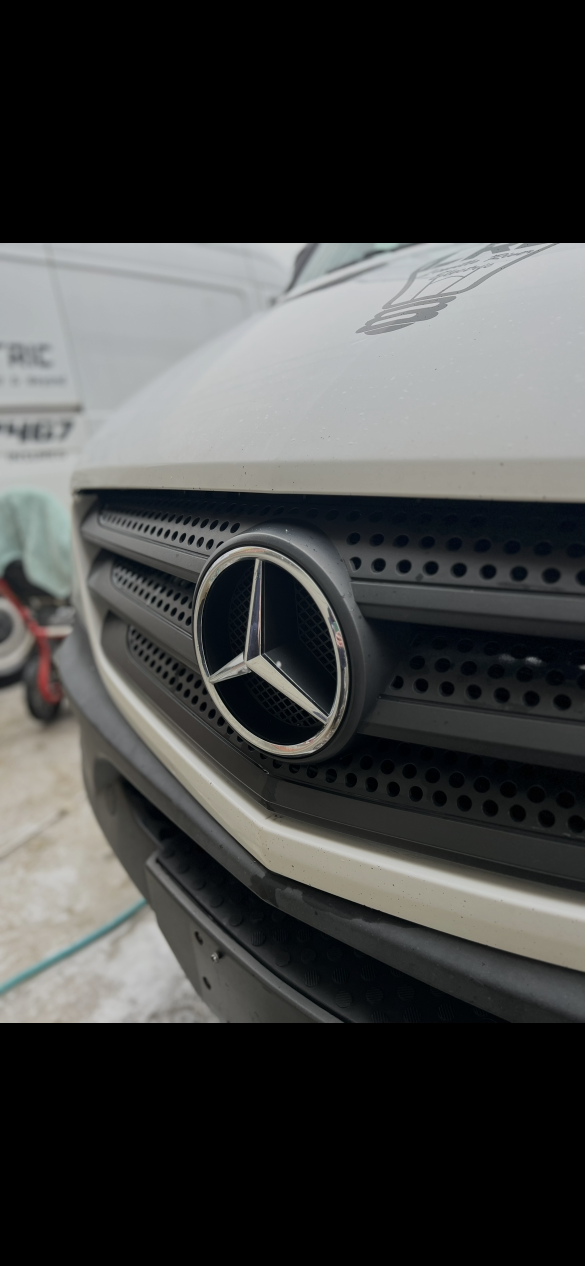 Close-up of the front grille of a white Mercedes-Benz vehicle, showing the Mercedes emblem.