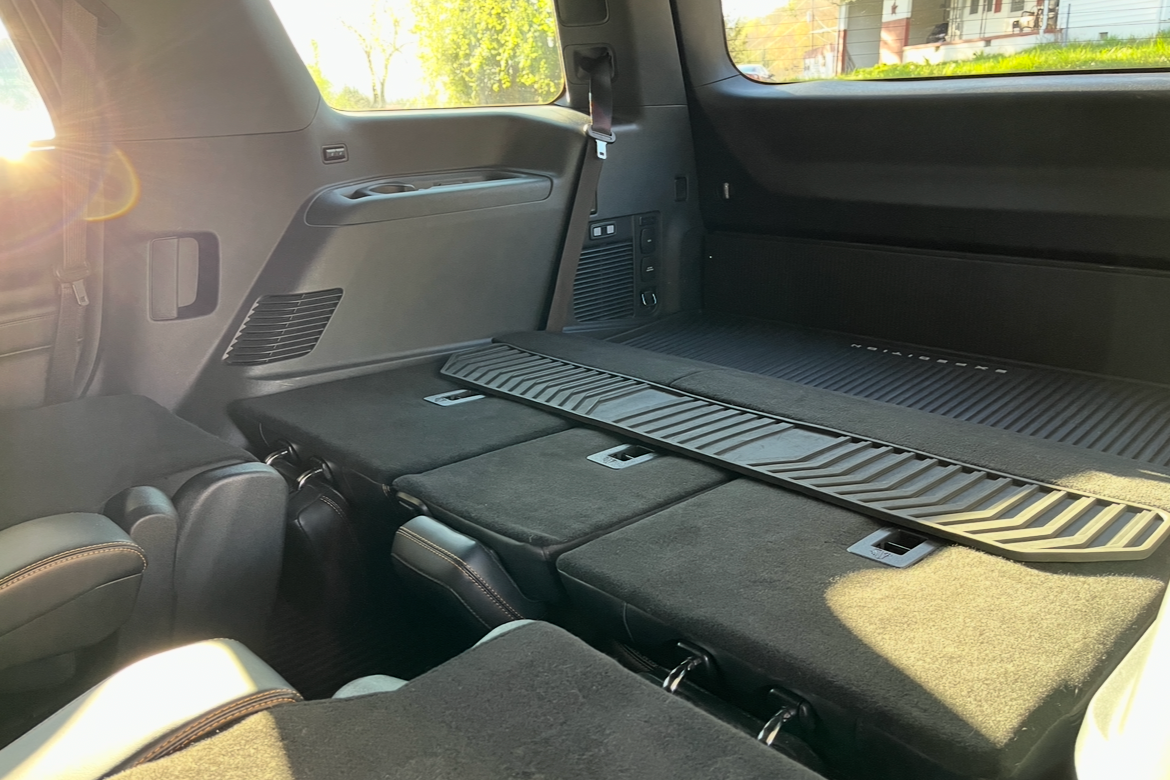 Interior of an SUV showing the folded down third-row seats with a cargo foldable cargo liner on top, sunlight coming in through the windows.