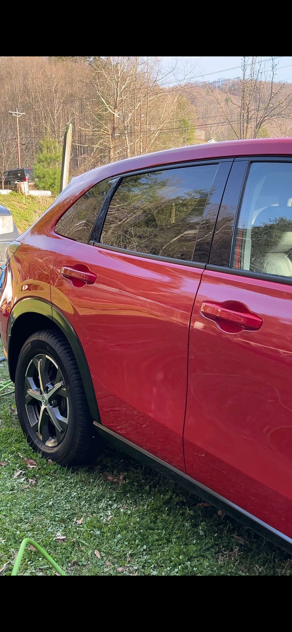 Close-up of a red SUV parked on grass, with trees and hills in the background.