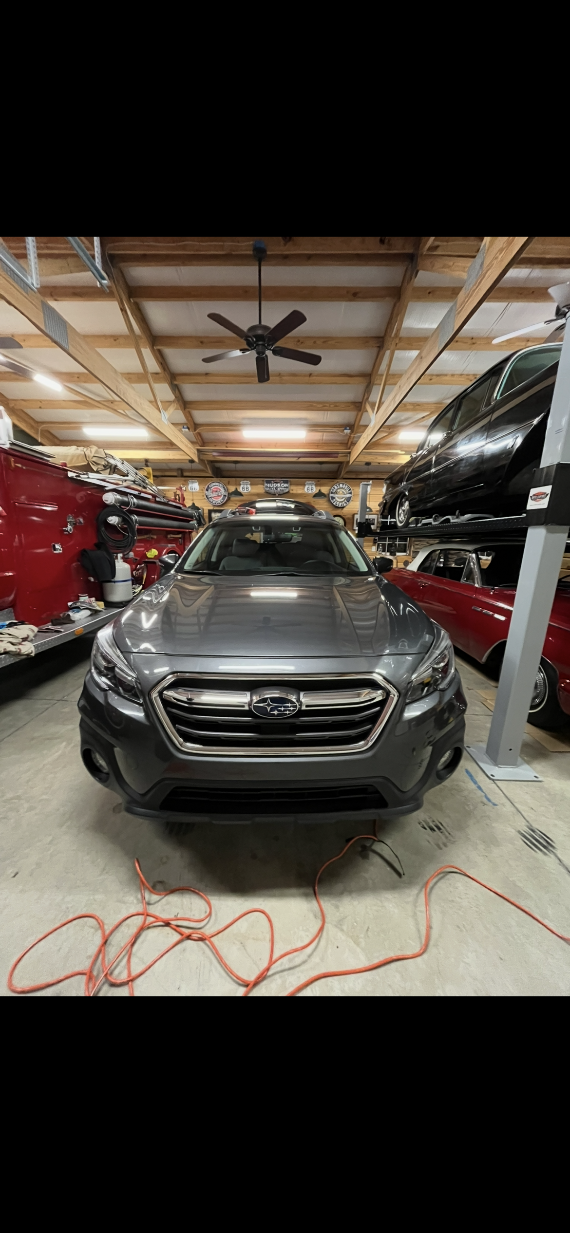 Gray Subaru SUV in a garage with vintage cars, tools, and memorabilia.