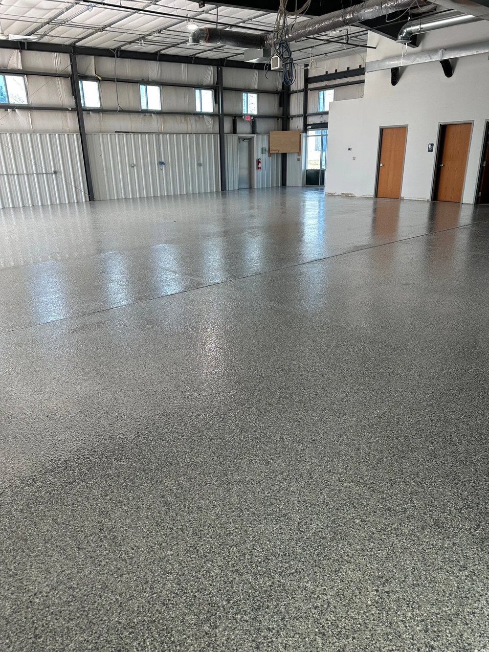 Gray decorative chip floor installed by Fortress Floors KC in an Olathe commercial interior with exposed steel framing and ductwork