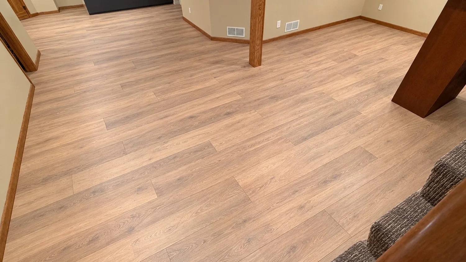 Light oak-look luxury vinyl plank flooring across a basement room with wood trim and a support post