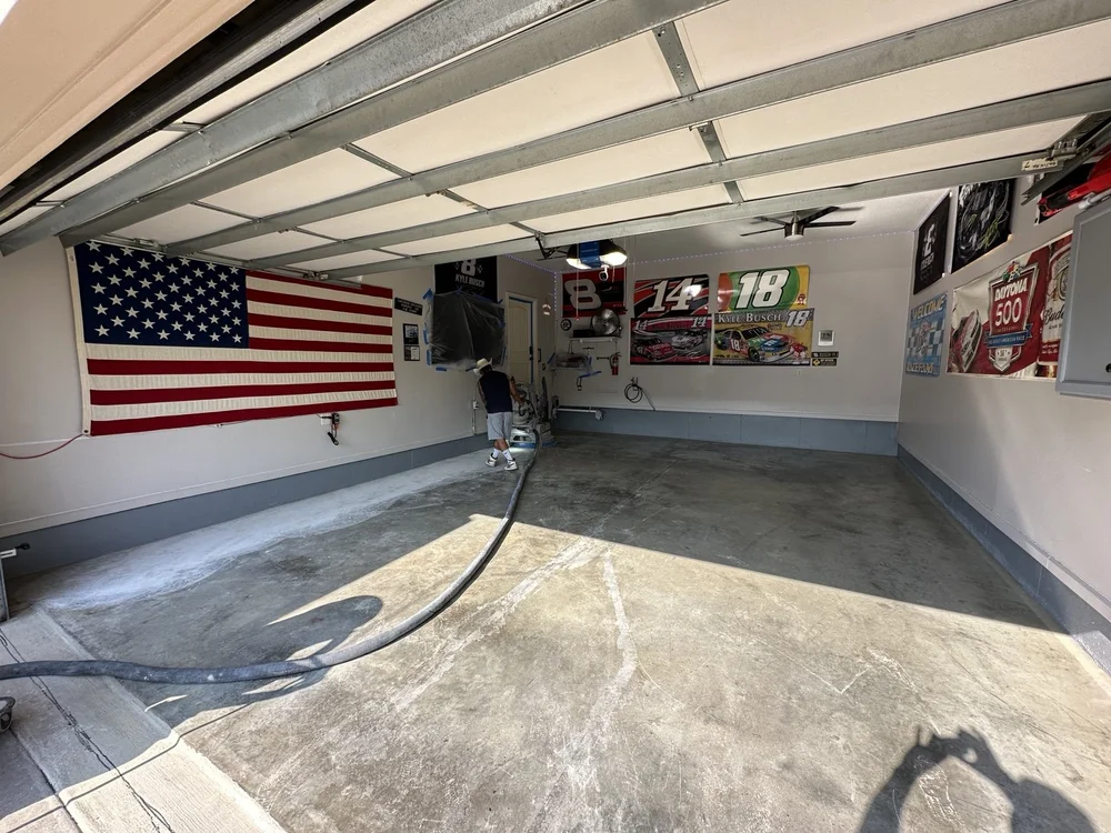 Grinding equipment and hose on a garage floor beneath an American flag and racing displays in Lee’s Summit