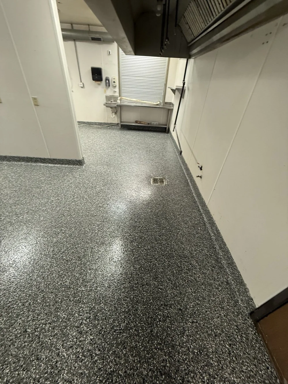 Finished decorative-chip commercial kitchen floor around a drain, facing a sink and pass-through
