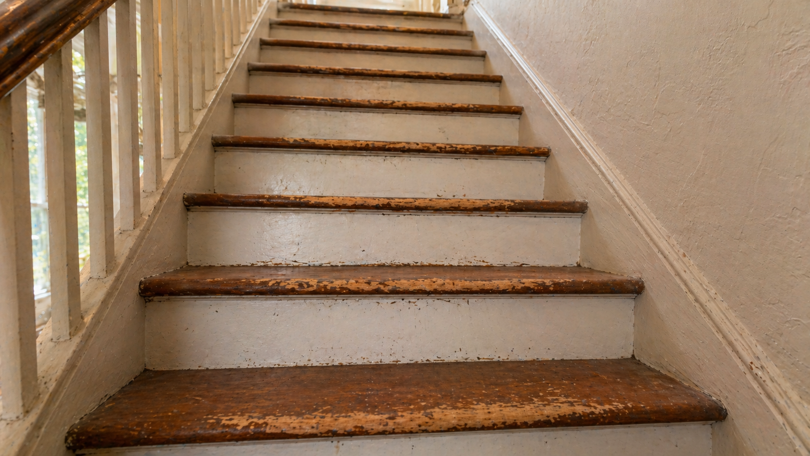 Worn red oak staircase in a Kansas City home with peeling finish and damaged nosings ready for refinishing