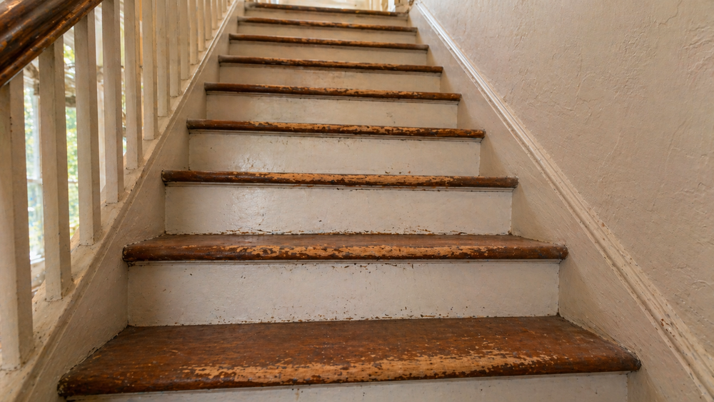 Wood stair treads with worn finish along the front edges and painted risers