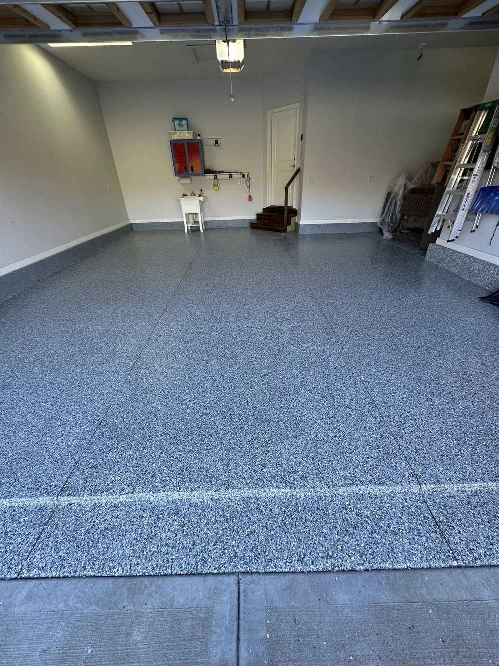 Finished garage floor and coated wall bases beside wooden steps and a utility sink in Liberty