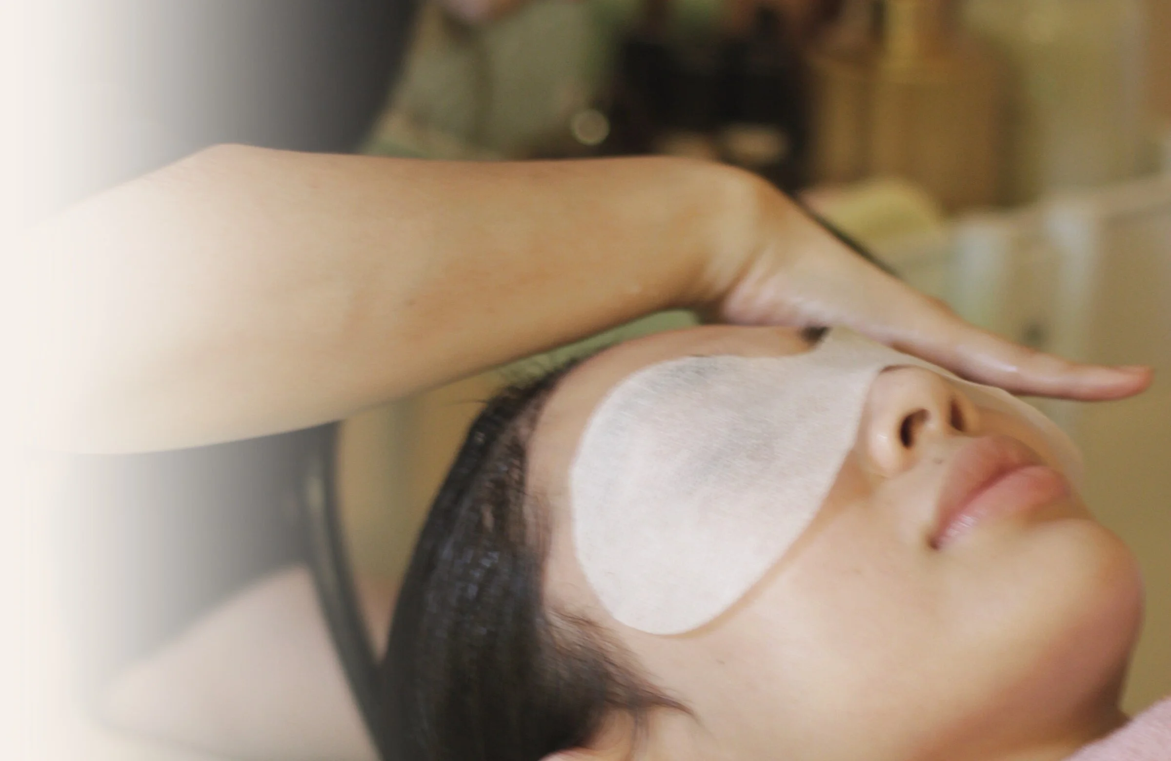 A practitioner's hand rests above a guest's eye pad during a head spa treatment
