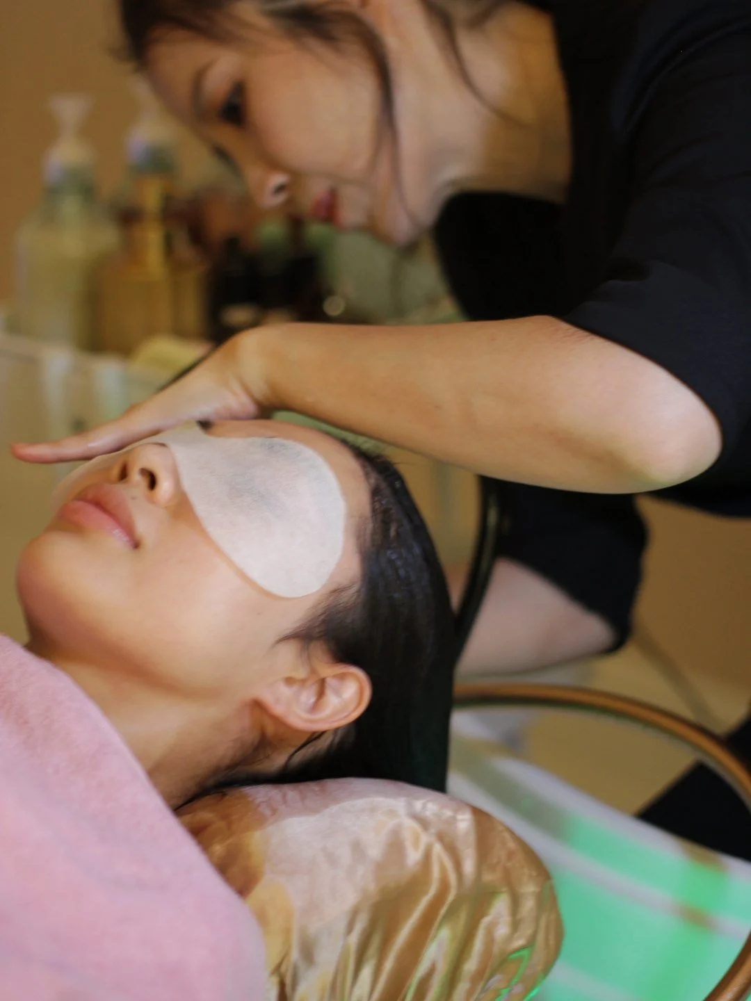 A therapist places an eye pad on a guest at the head spa basin