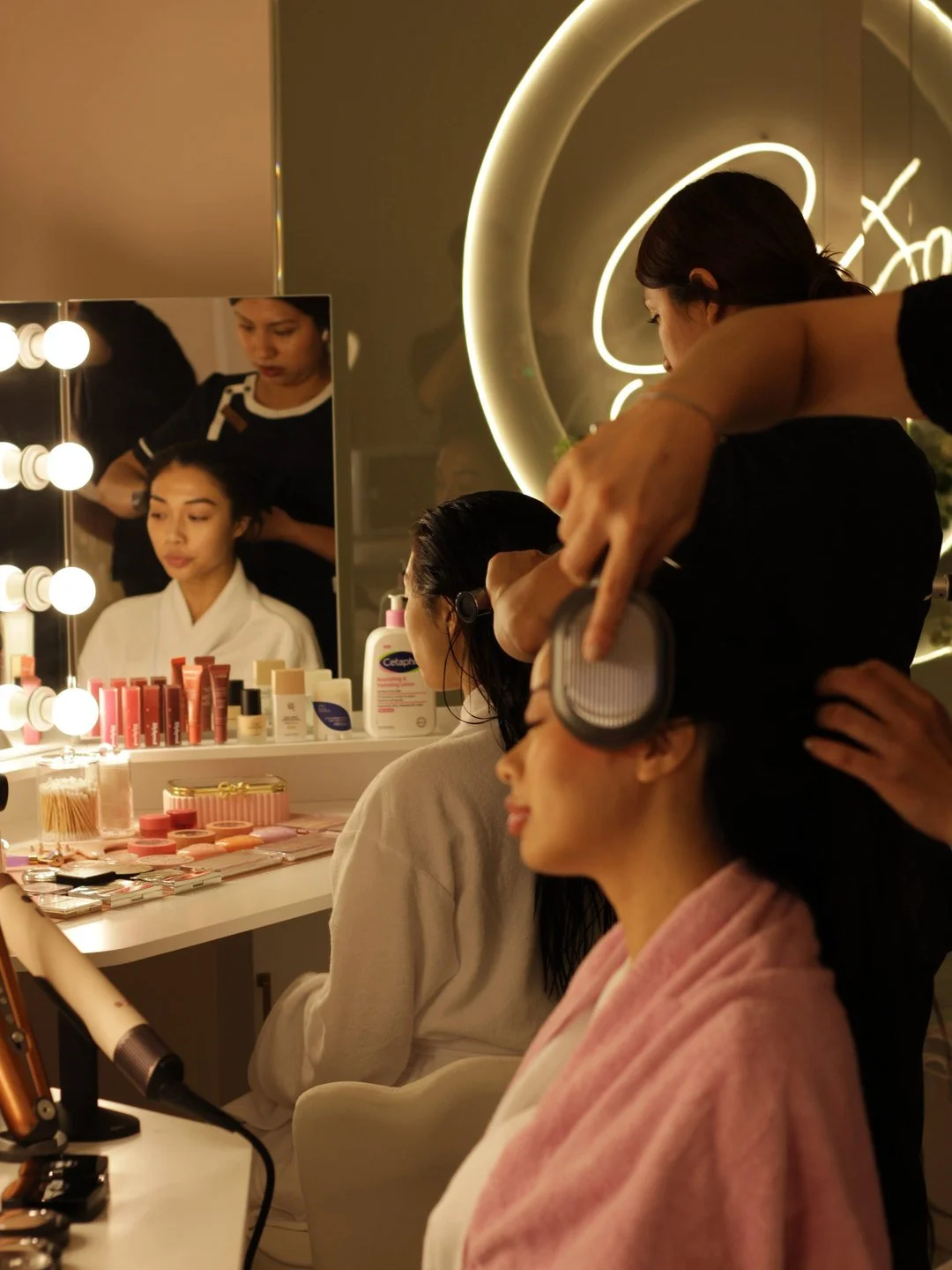 A stylist works on a guest's hair at lit makeup mirrors