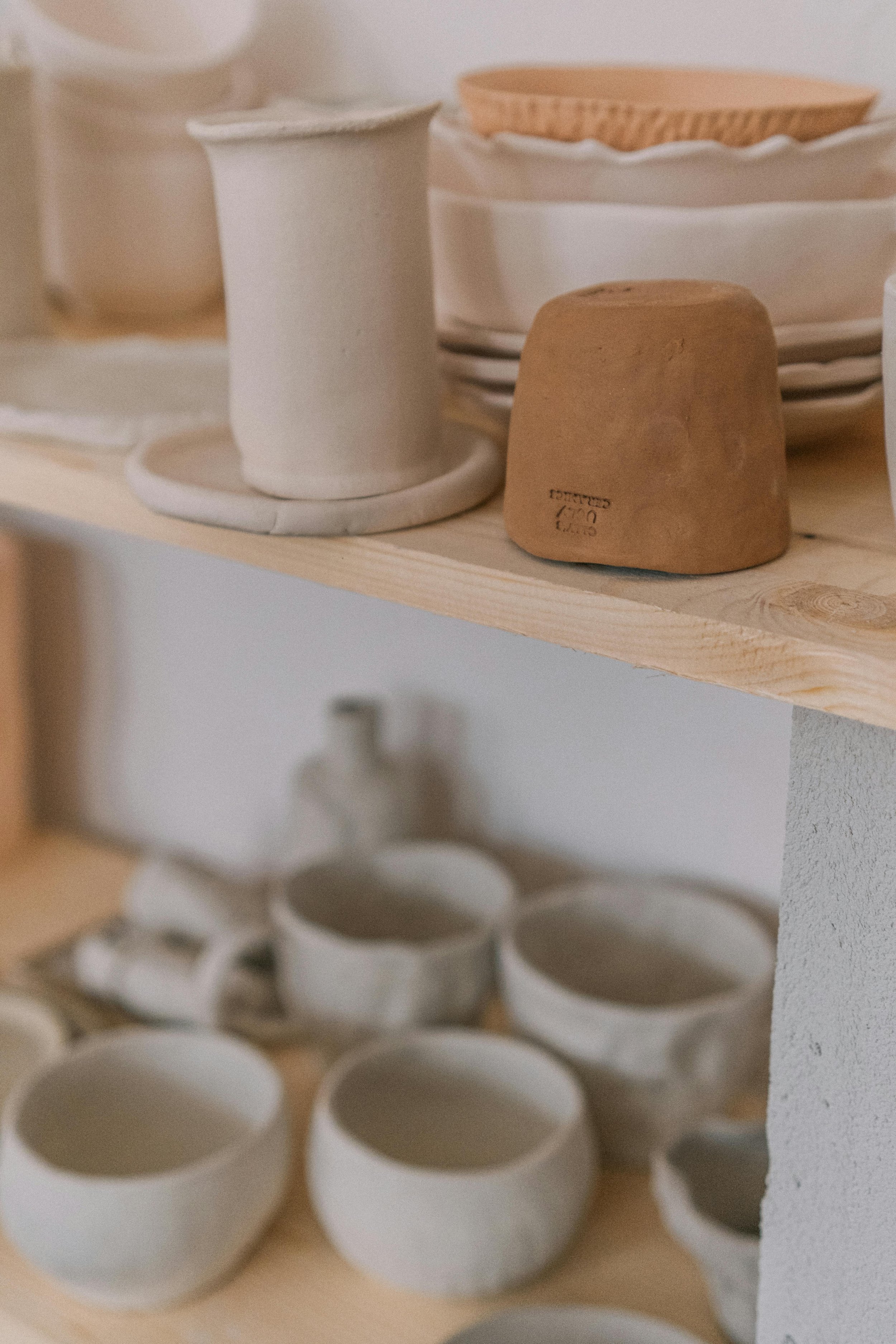 Stacked white and beige ceramic bowls, cups, and plates on wooden shelves in a kitchen setting.