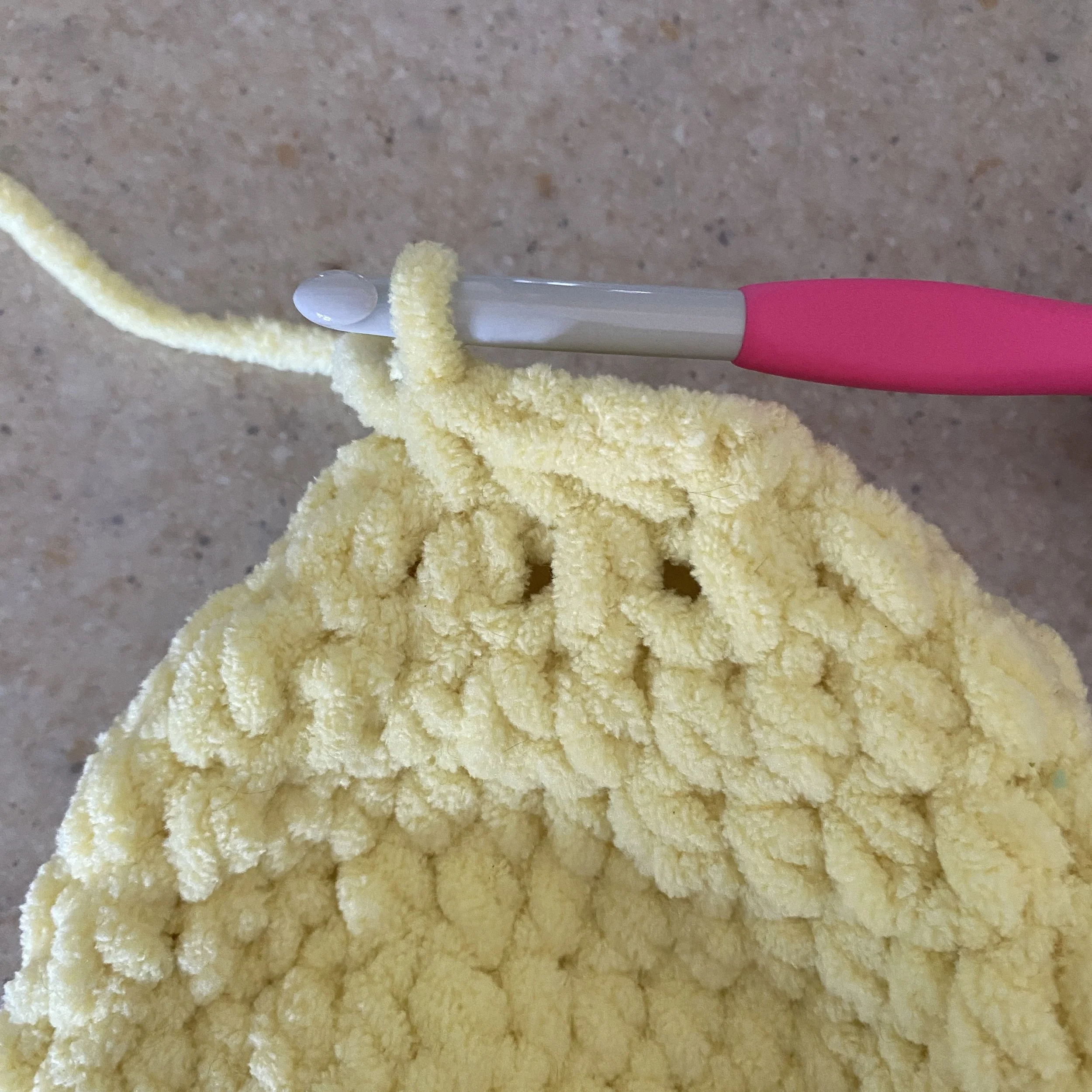 Close-up crochet tutorial photo showing stitch placement while closing the plush lemon body for the Lila the Lemon Lovey crochet pattern using bulky yellow yarn.