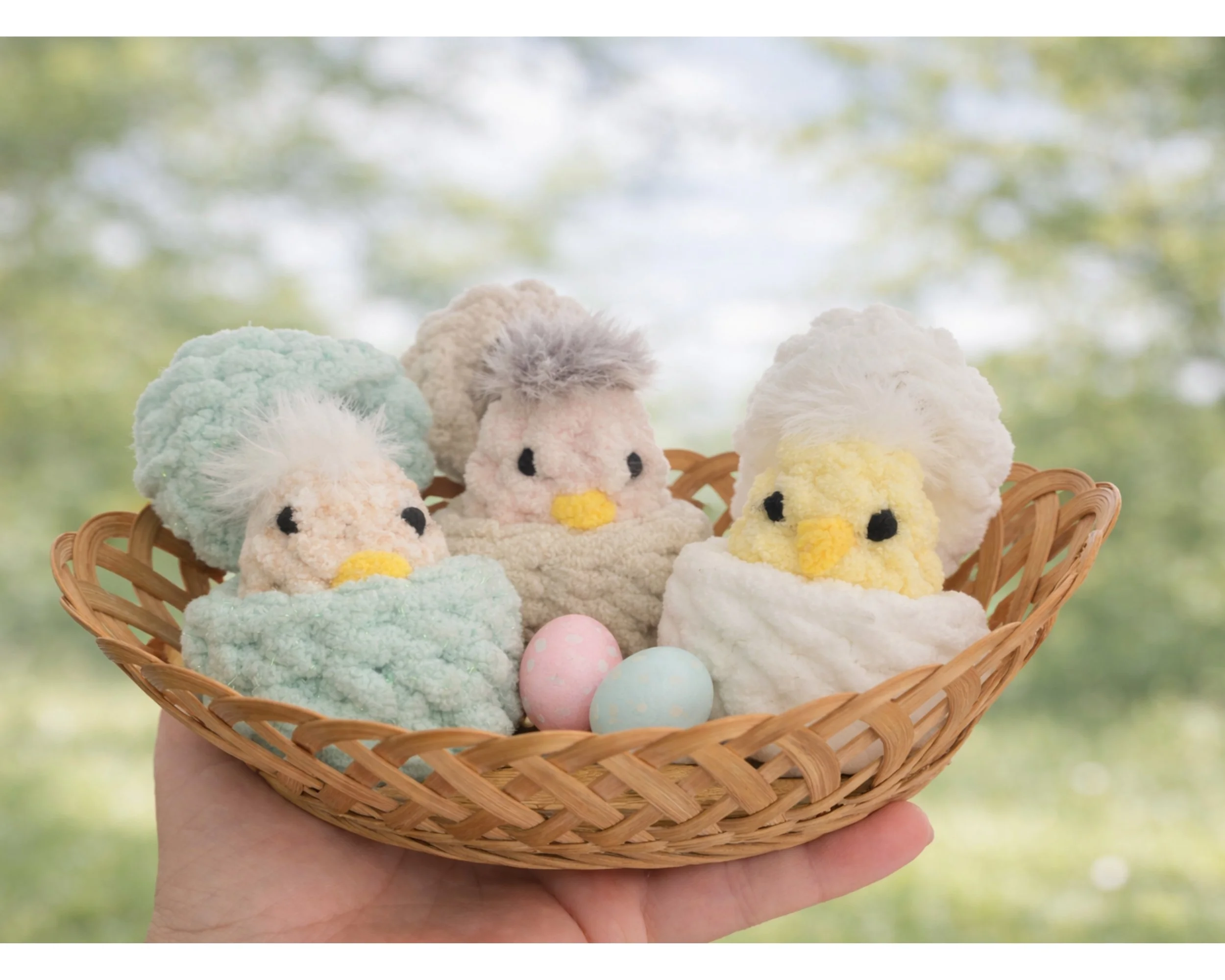 Crocheted peek-a-boo chicks sitting in a small woven basket with pastel eggs, linking to the Peek-a-Boo Chick crochet pattern.