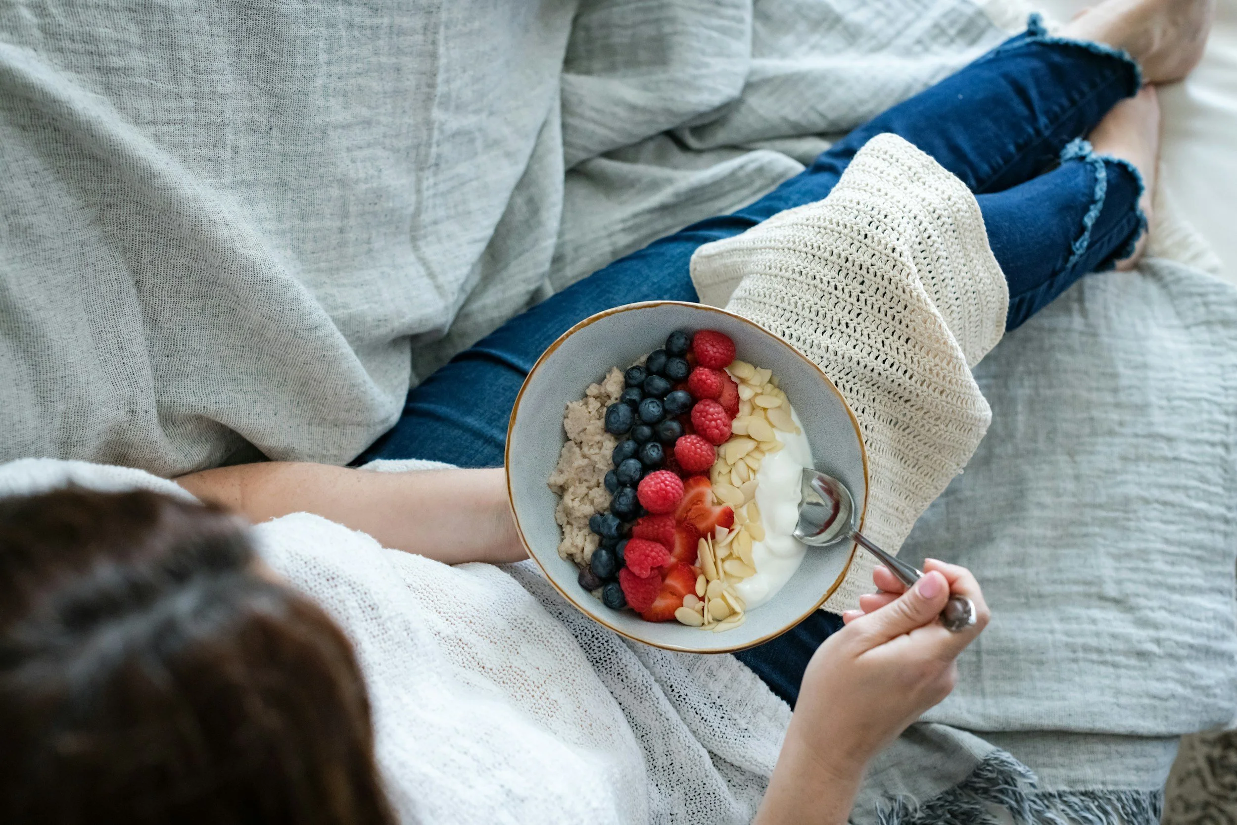 Person holding a bowl of yogurt topped with blueberries, raspberries, strawberries, sliced almonds, and granola.
