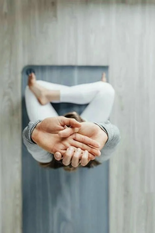 Person lying on a bed with hands clasped behind head, viewed from above.