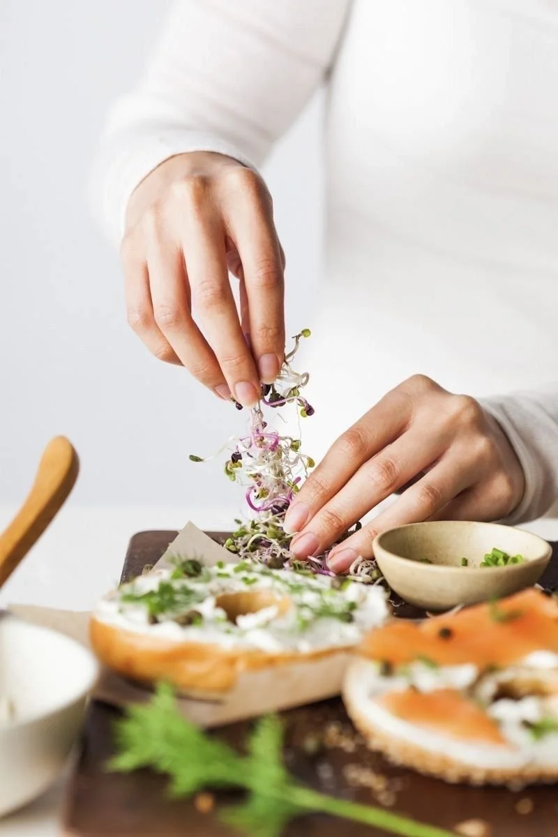 Person garnishing a dish with microgreens on a wooden cutting board.