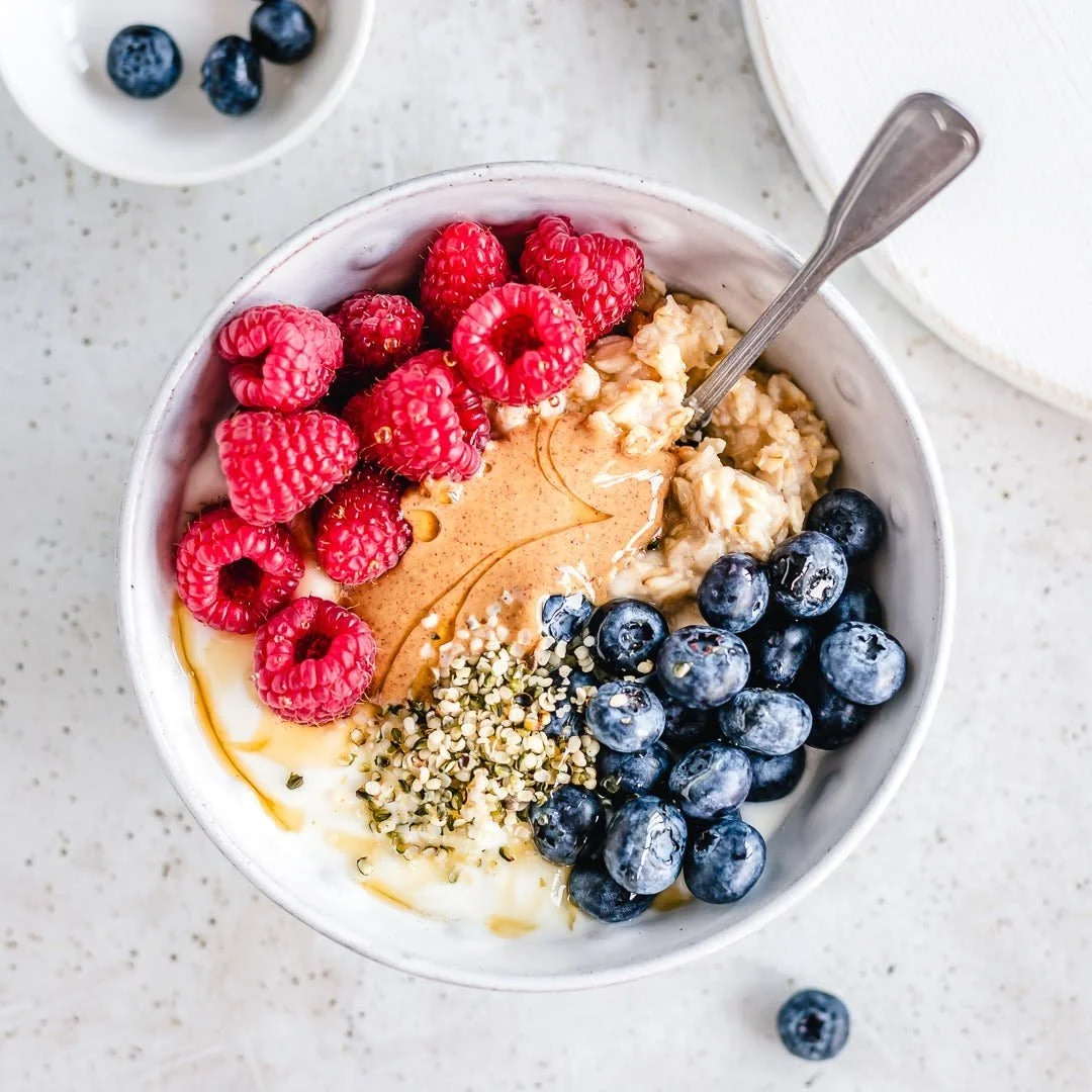 A bowl of oatmeal topped with raspberries, blueberries, hemp seeds, and a drizzle of honey.