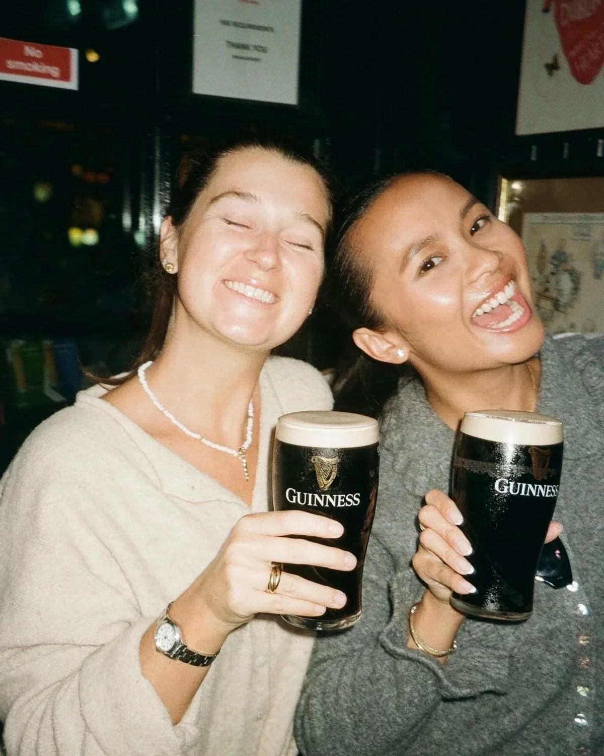 2 girls holding pints of Guinness posing for photos on a night out in a UK pub