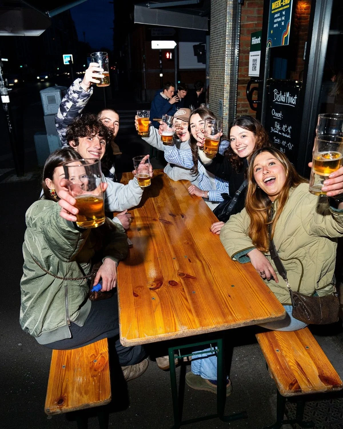 a group at a table in a bar, holding their beers out in a cheers motion