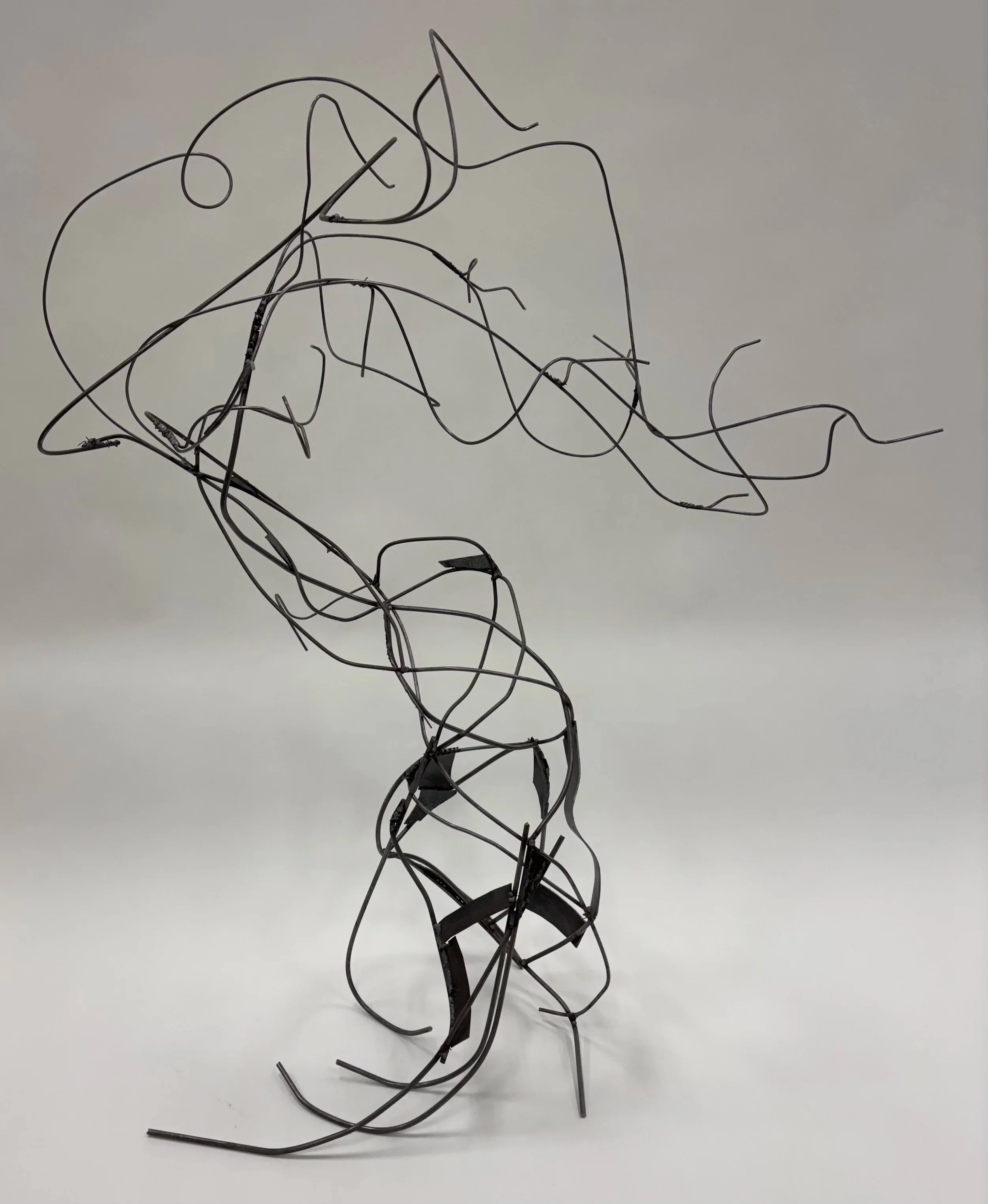 Abstract sculpture made of intertwined black metal wires, resembling a human figure, on a plain white background.