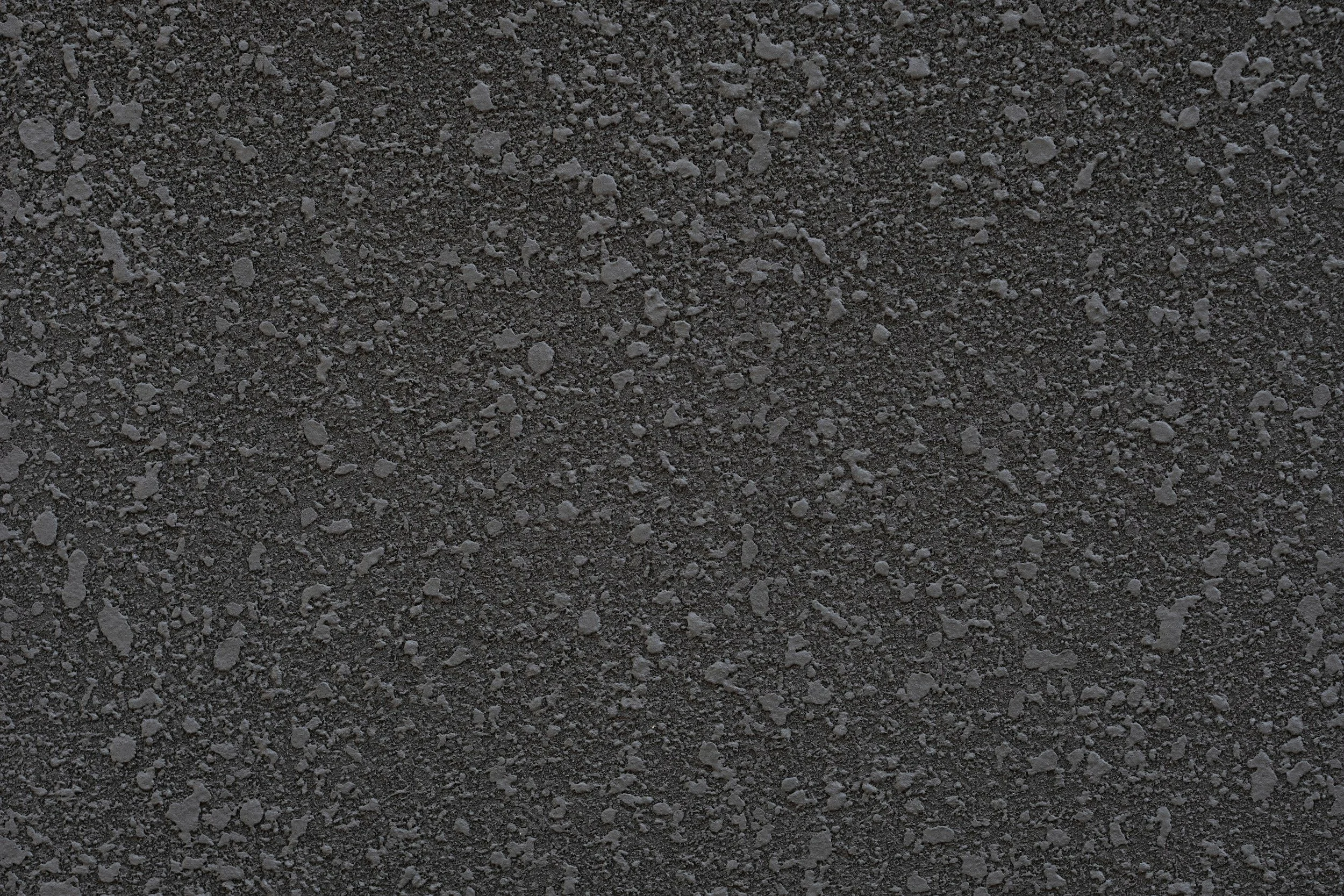 Close-up view of a rough, dark asphalt surface with small pebbles and gravel embedded.
