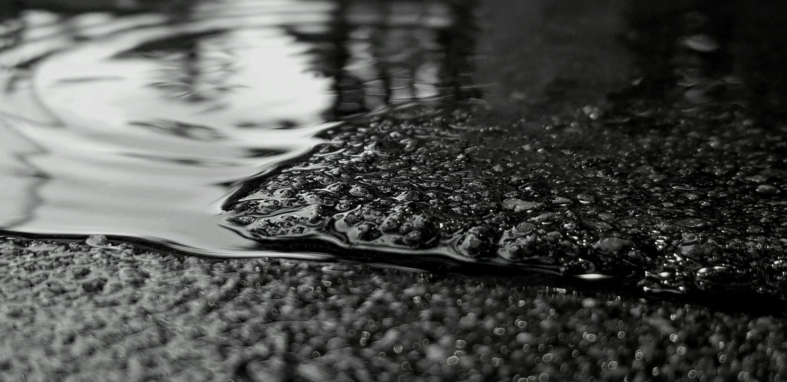 Close-up of a puddle with ripples on a dark, textured surface.