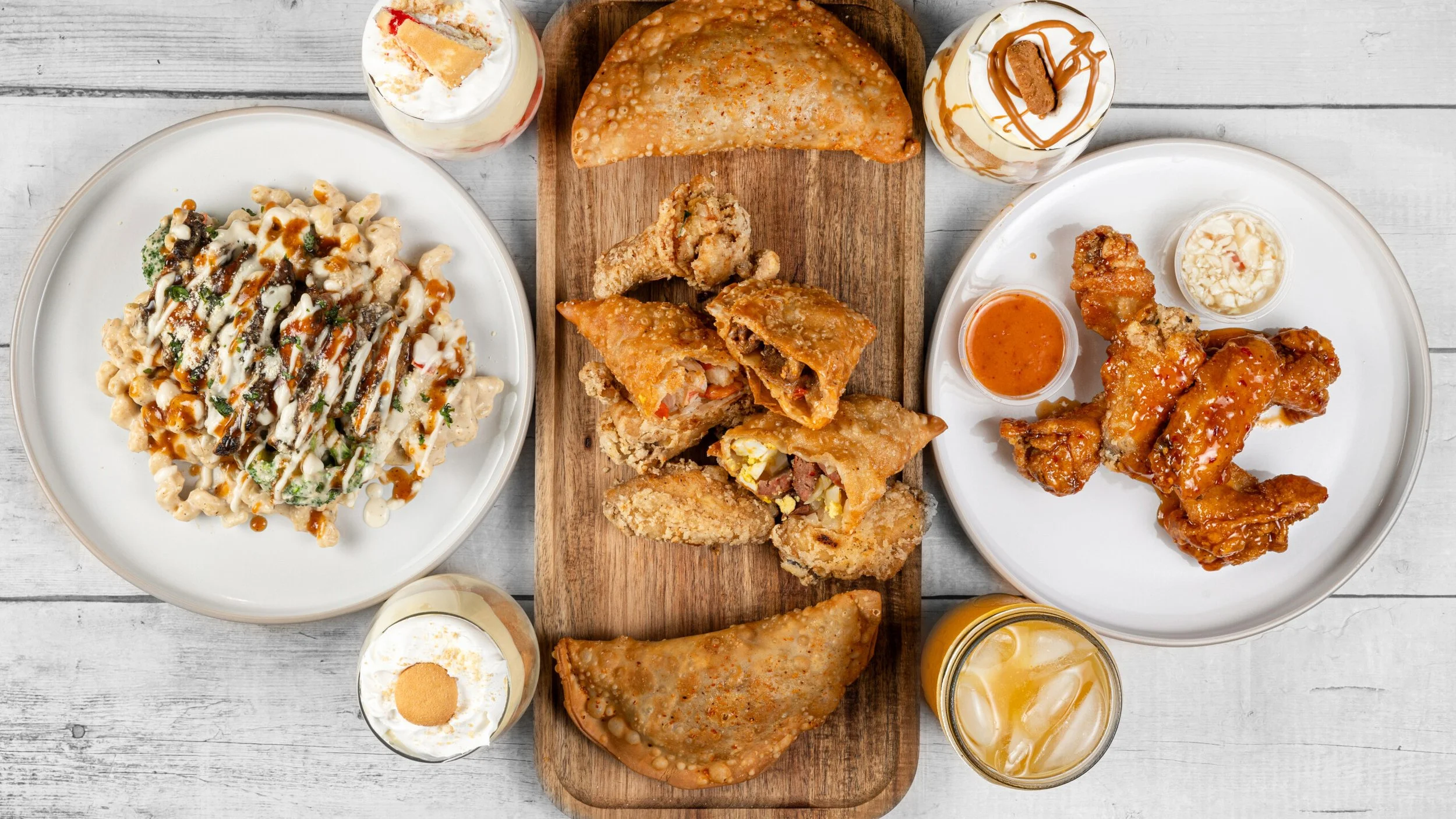 Palate Bomb Haitian & American fusion food spread featuring patties, wings, creamy pasta, desserts, and fresh drinks.