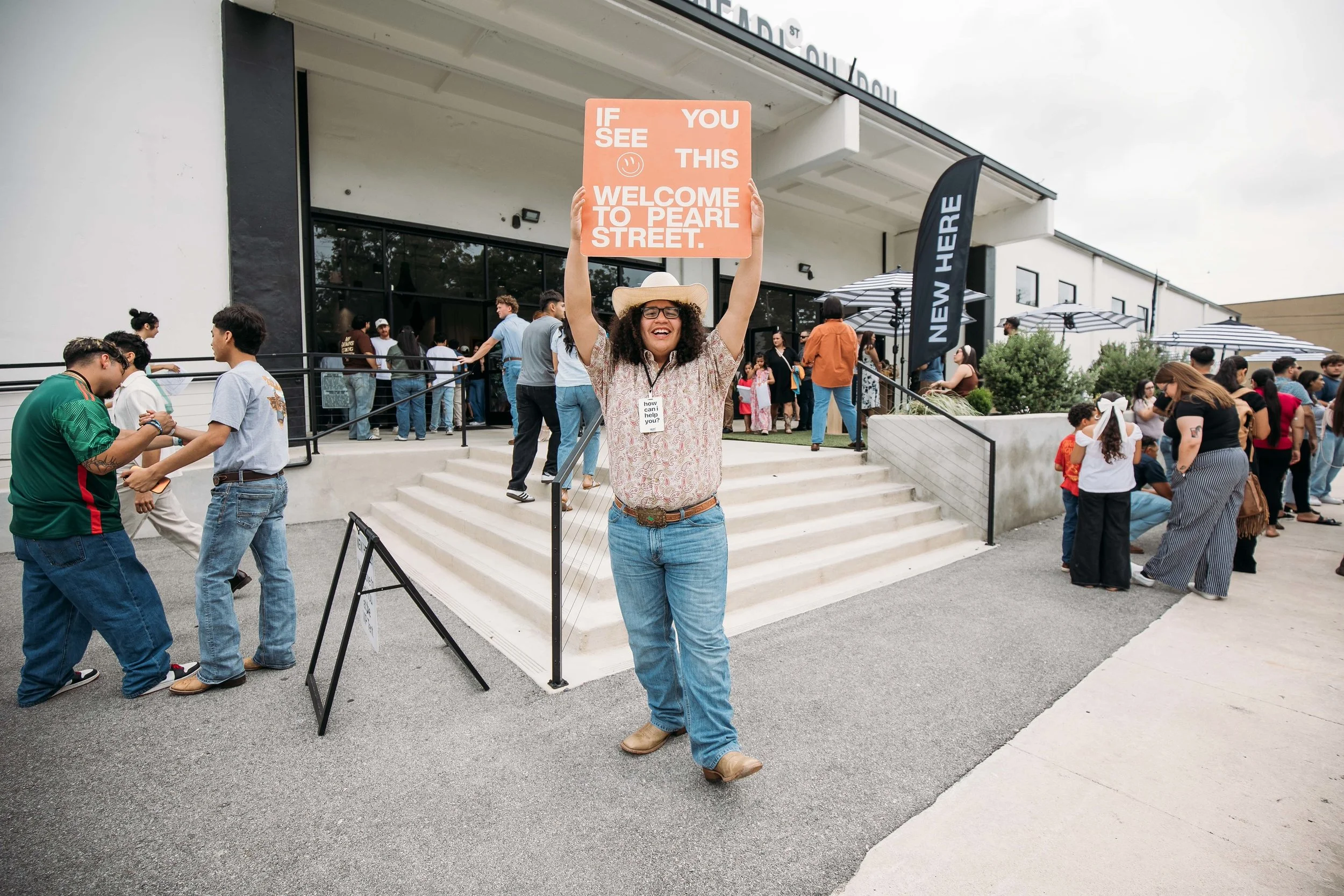 Welcome Team volunteer holding a "Welcome to Pearl Street" sign outside Pearl Street Church Downtown in San Antonio