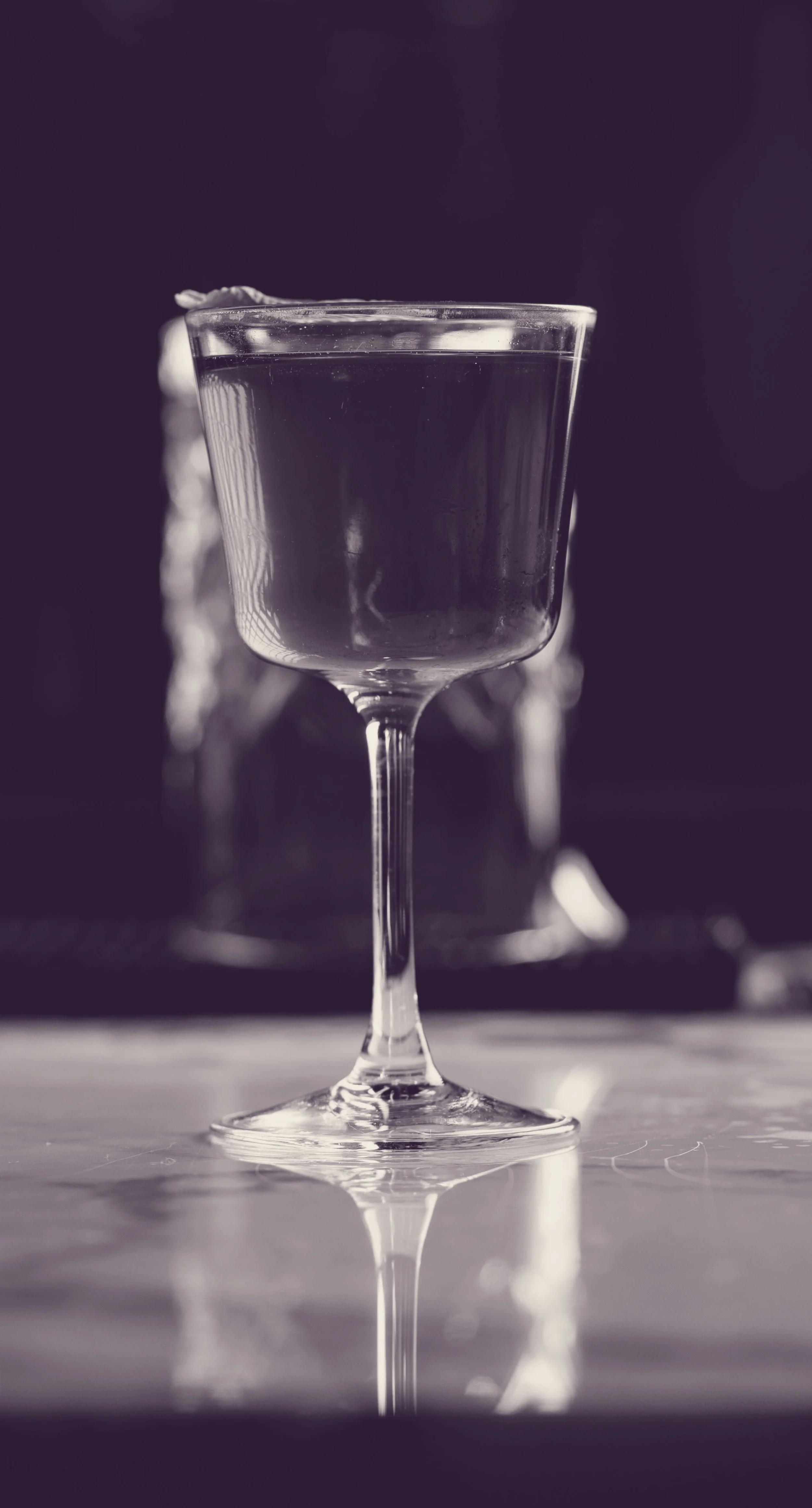 A close-up black and white photograph of a wine glass filled with water, with a blurred background.