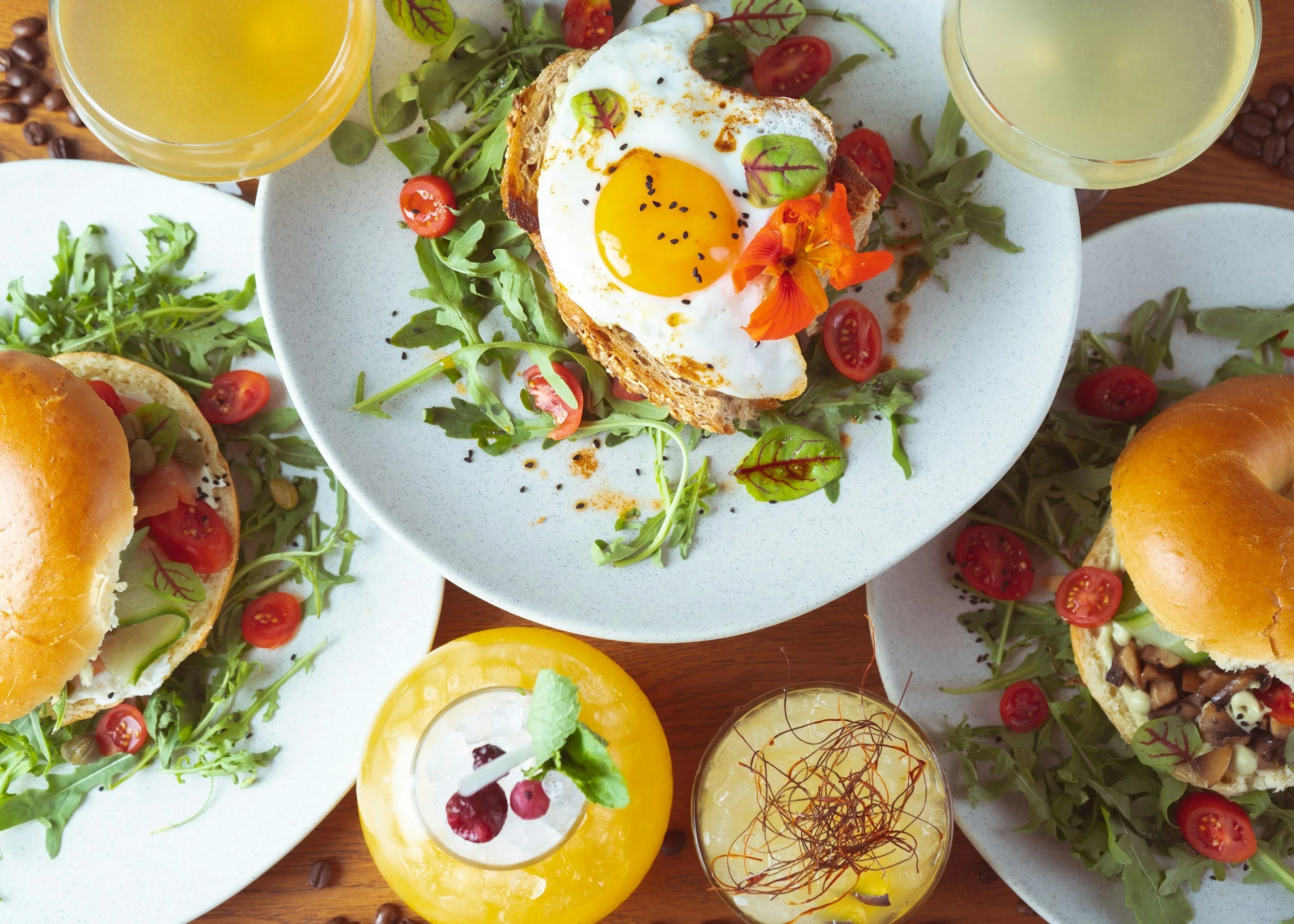 A table with various dishes including a croissant with berries on a white plate, slices of toasted bread, a salad with greens and cheese, a glass of water, a cup of coffee, and small bowls of butter and sauce.