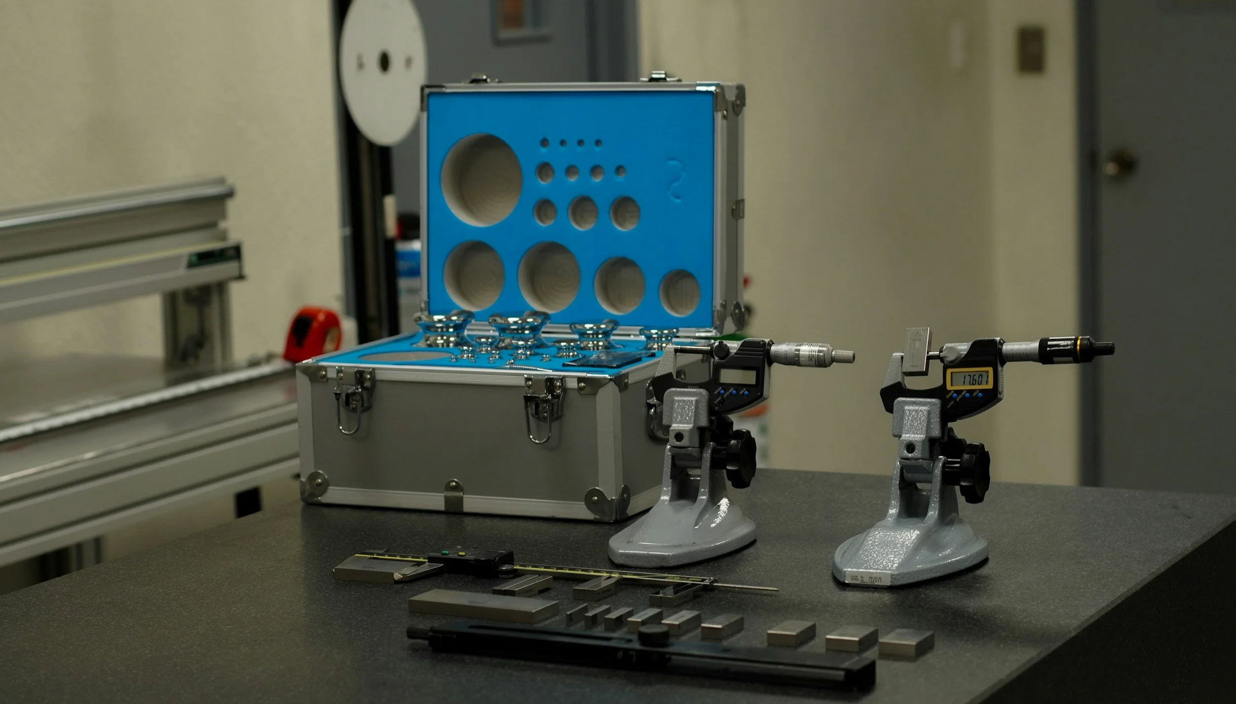 Laboratory setup with measurement instruments, a blue carrying case with circular holes, and various small metallic and black components on a black work surface in a clinical or research environment.
