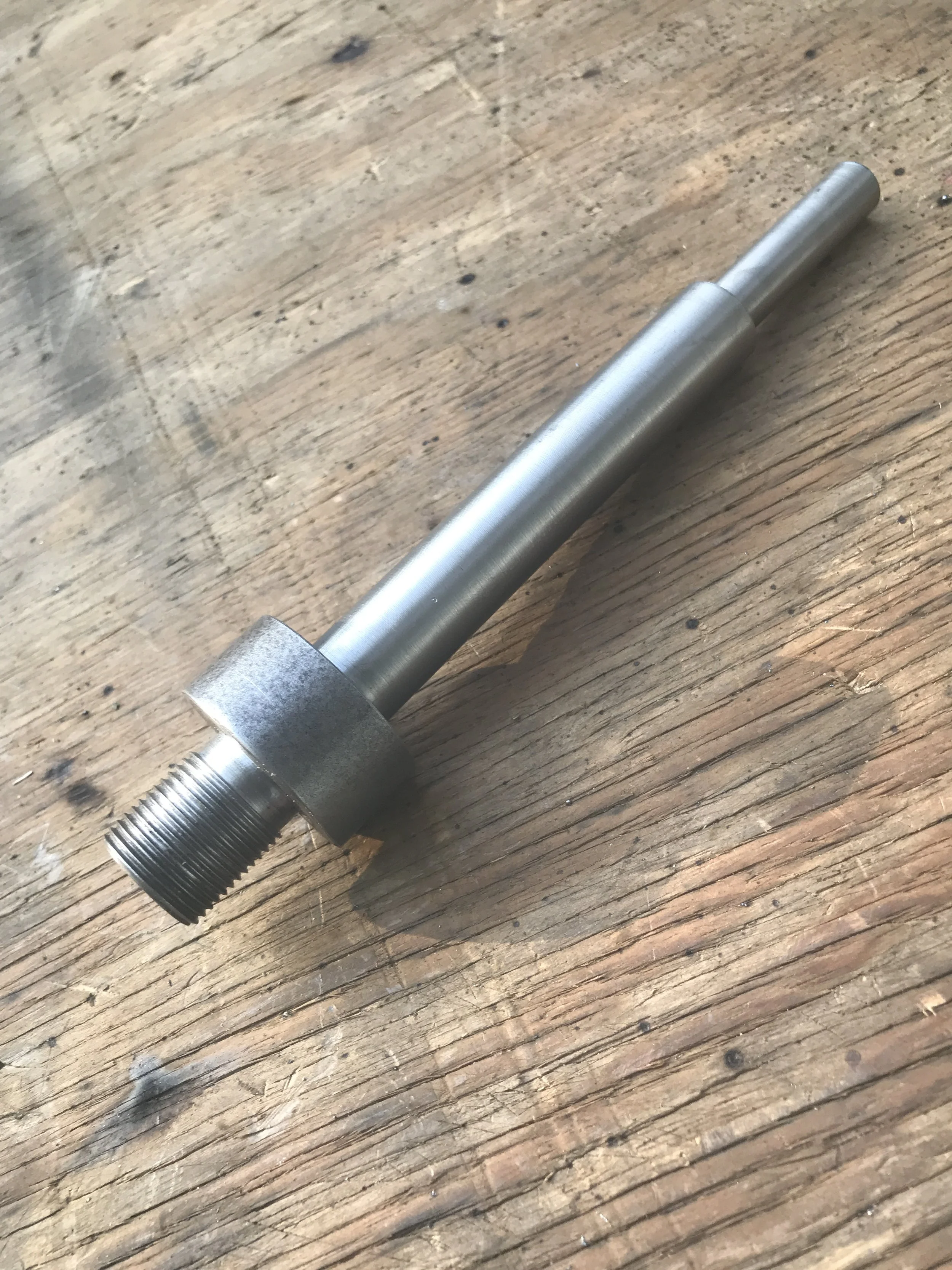 A metal rod with a threaded end and a hexagonal section, resting on a wooden surface.