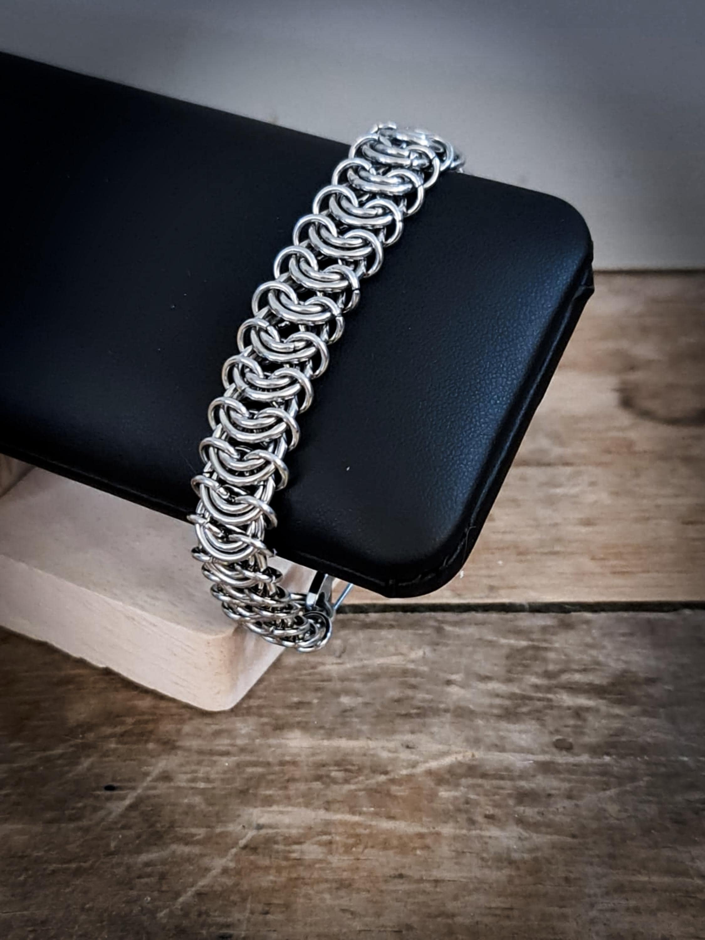 Silver chain necklace draped over a black jewelry display stand on a wooden surface.