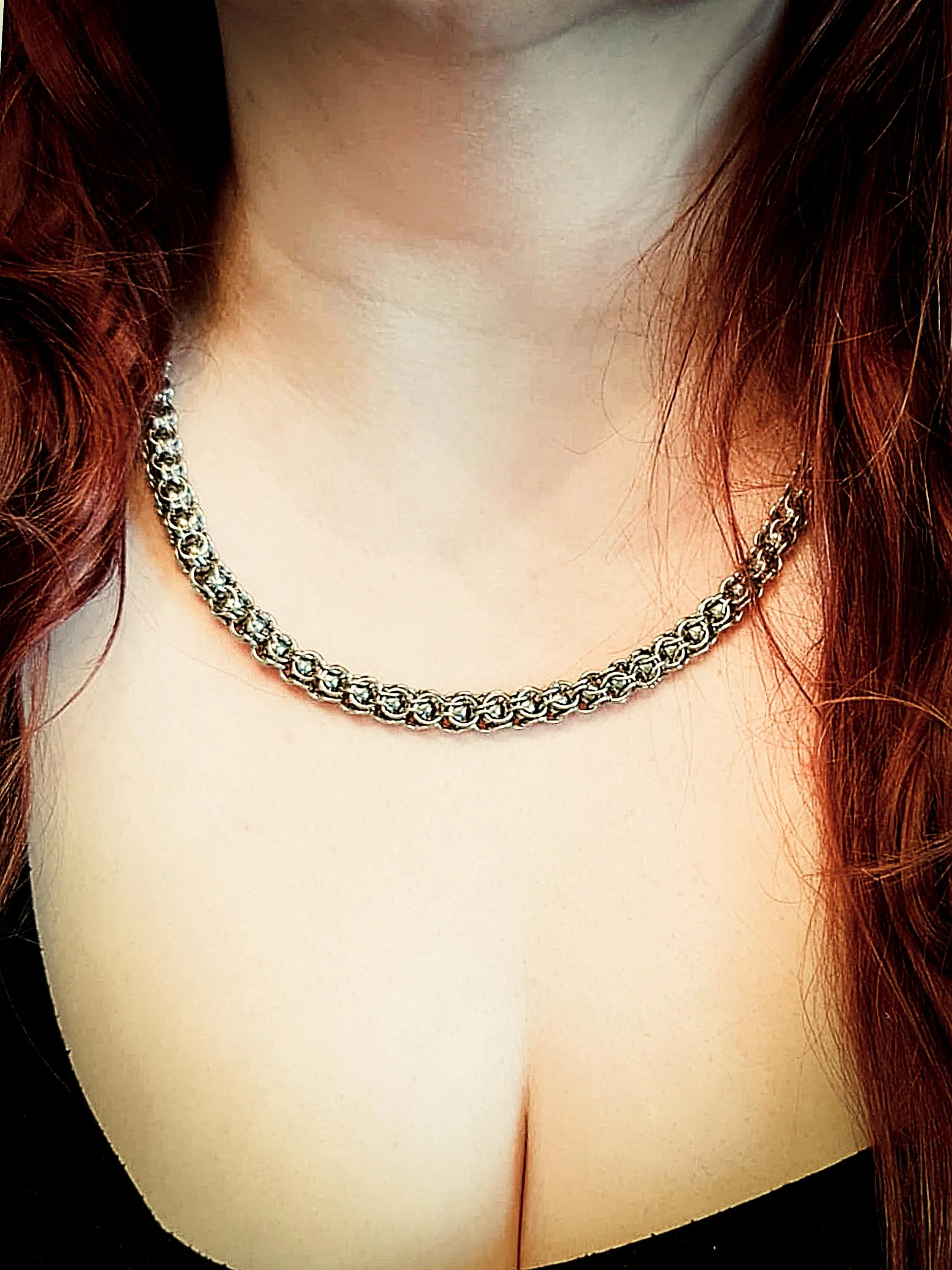 Close-up of a woman wearing a silver chain necklace and a black top, with long red hair.