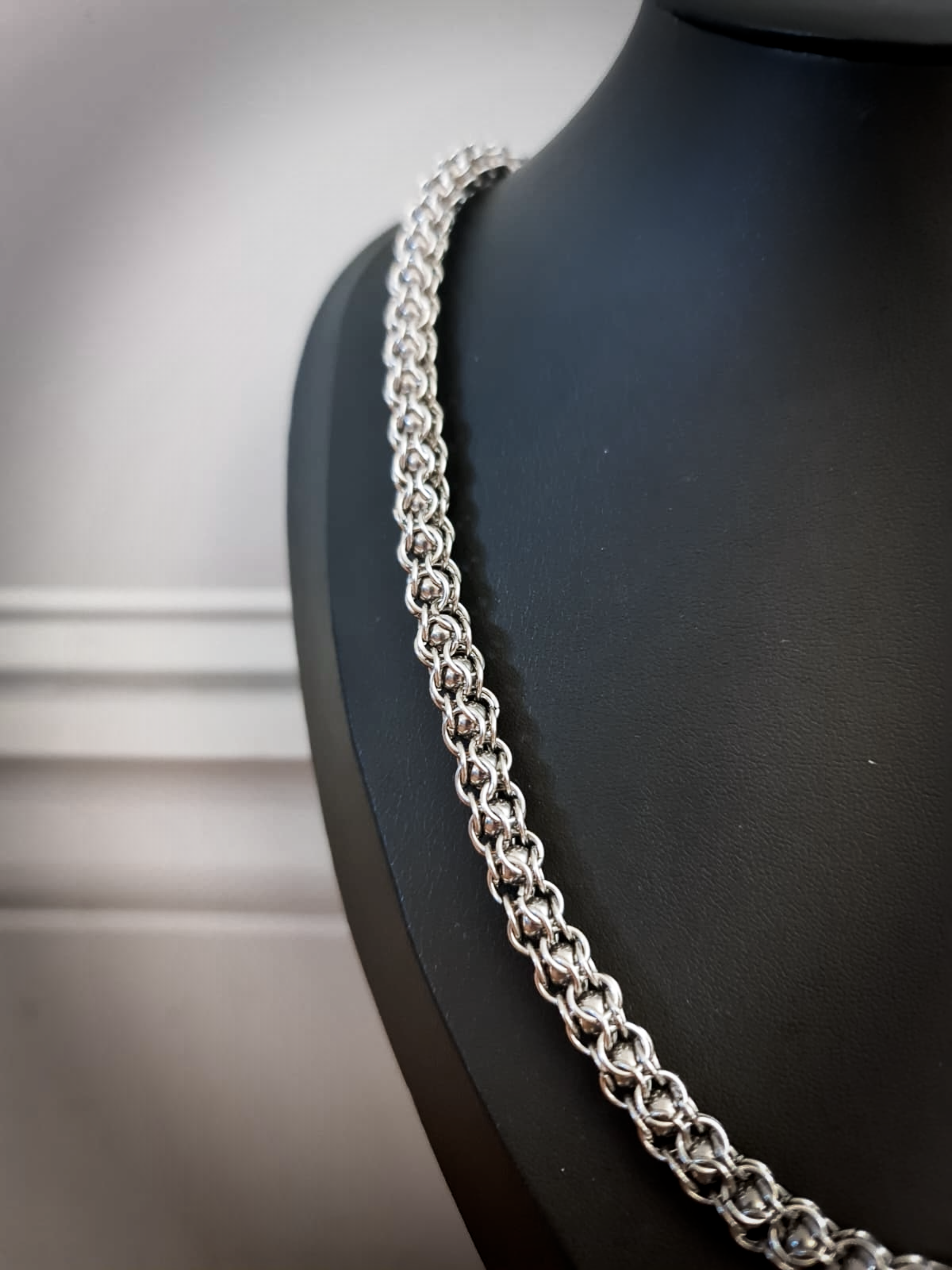 Close-up of a silver chain necklace displayed on a black jewelry stand.