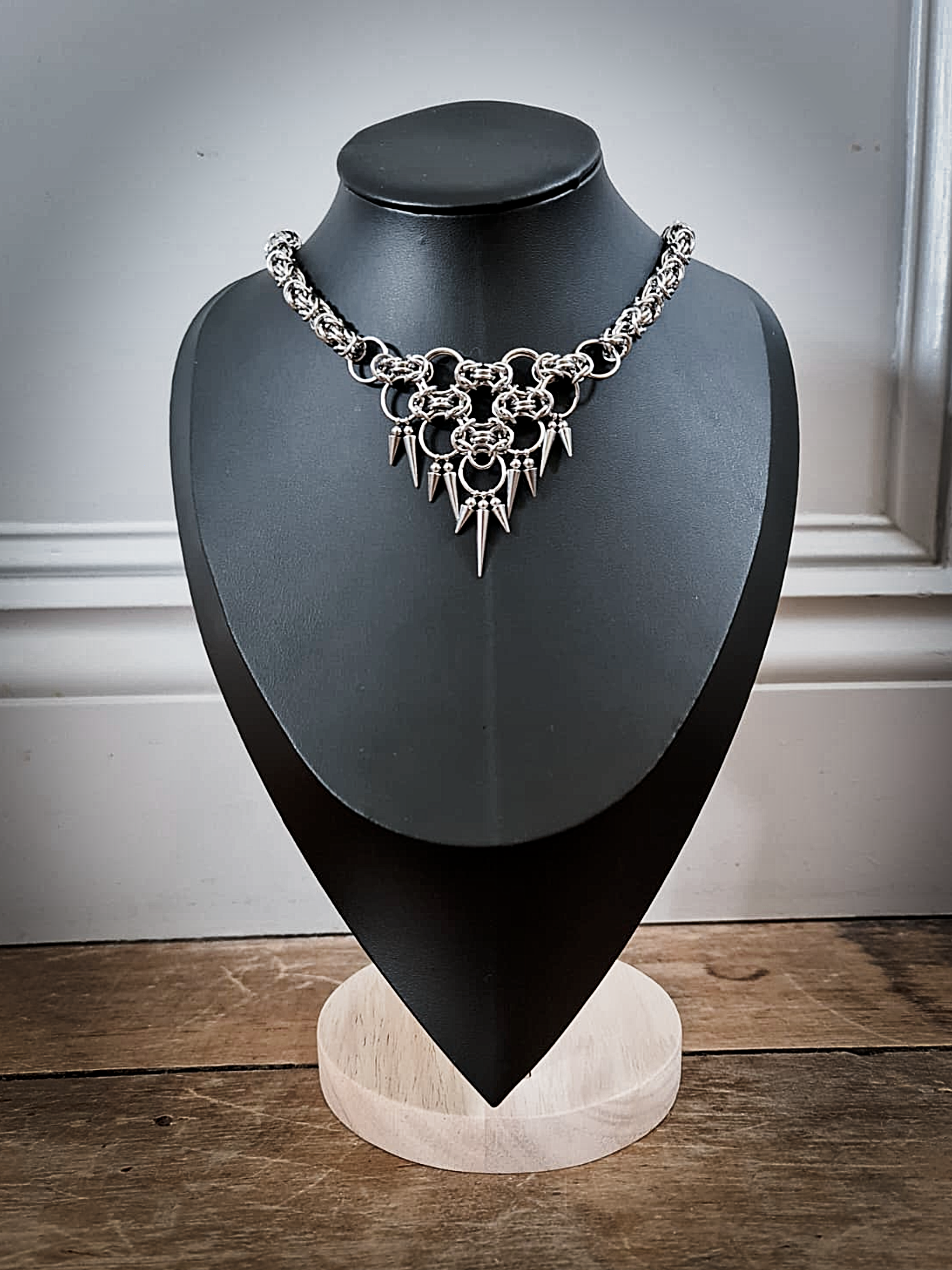 Silver statement necklace with spikes on a black display bust on a wooden surface.