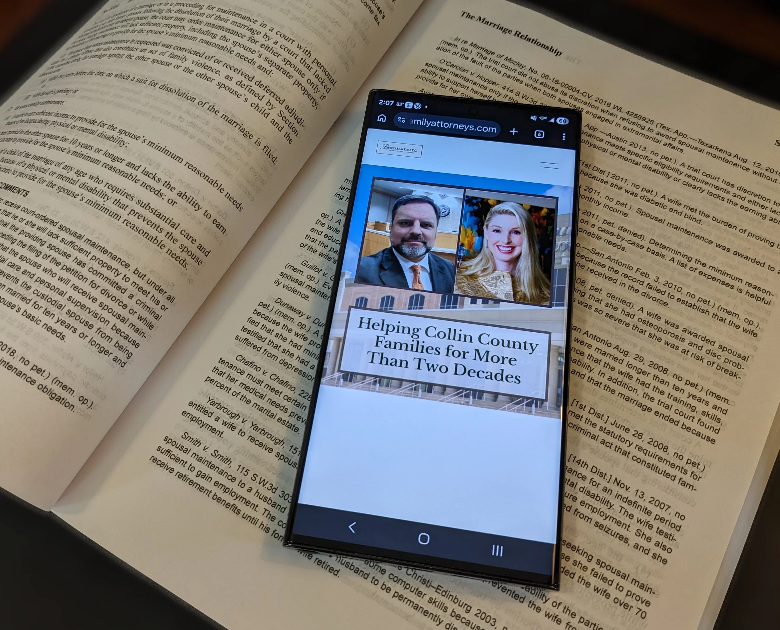 A smartphone displaying a webpage with pictures of a man and a woman dressed professionally. The background includes open legal books, focusing on legal text.