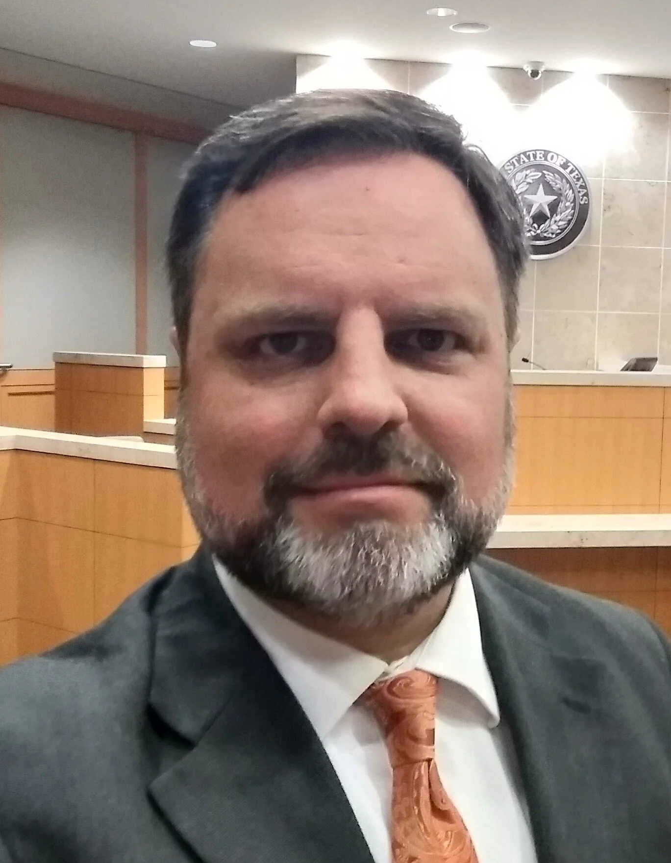 Eric LaFleur, an attorney in  a dark suit, white shirt, and orange tie, standing in a Collin County, Texas courtroom with a seal of the State of Texas in the background.