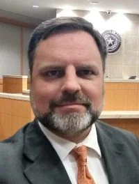 Attorney Eric LaFleur, wearing a suit and an orange tie, standing in a Collin County, Texas courtroom with the Seal of the State of Texas visible on the wall behind him.