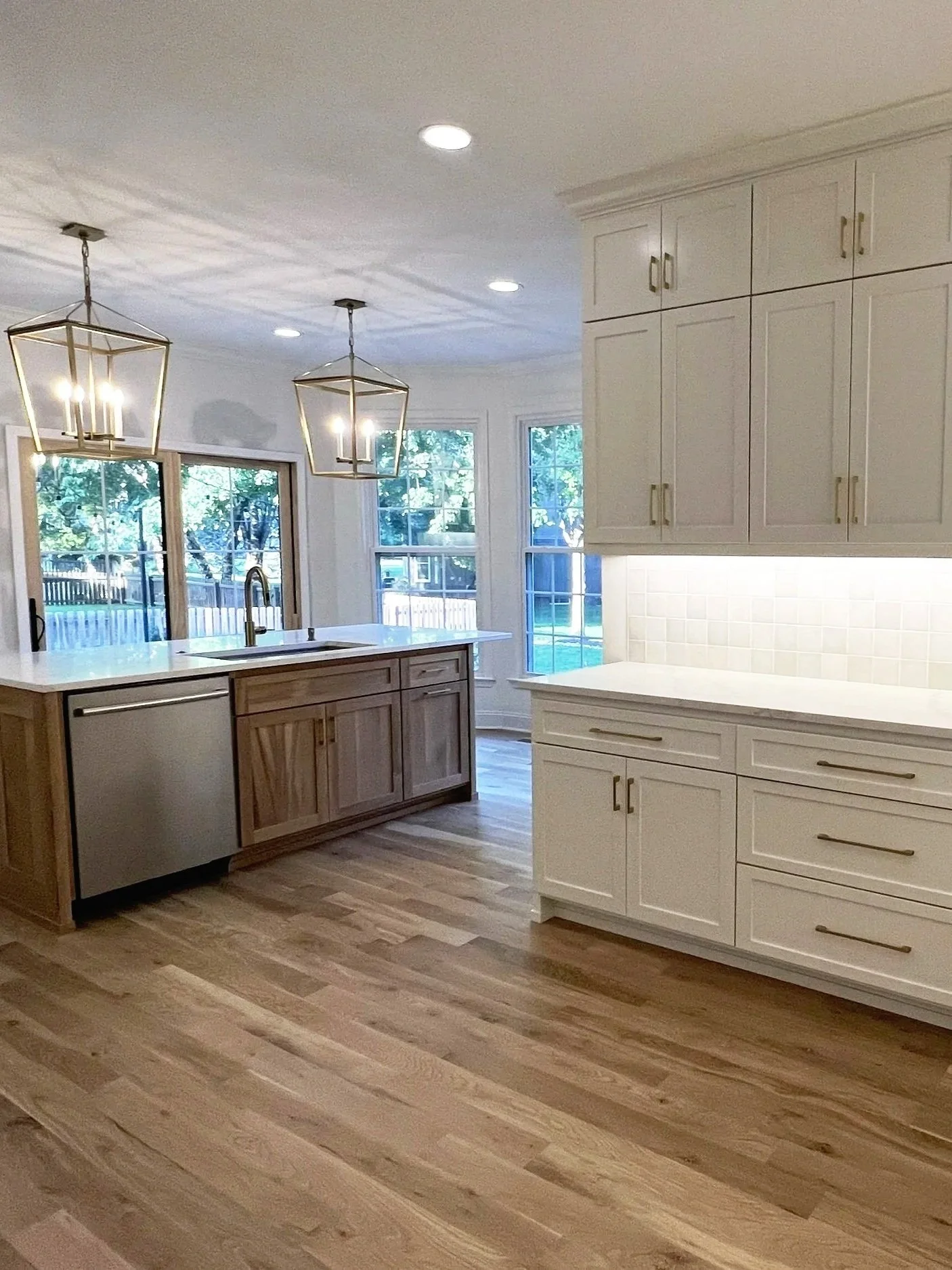 Modern kitchen with hardwood floors, white cabinets, a large window, and hanging light fixtures.
