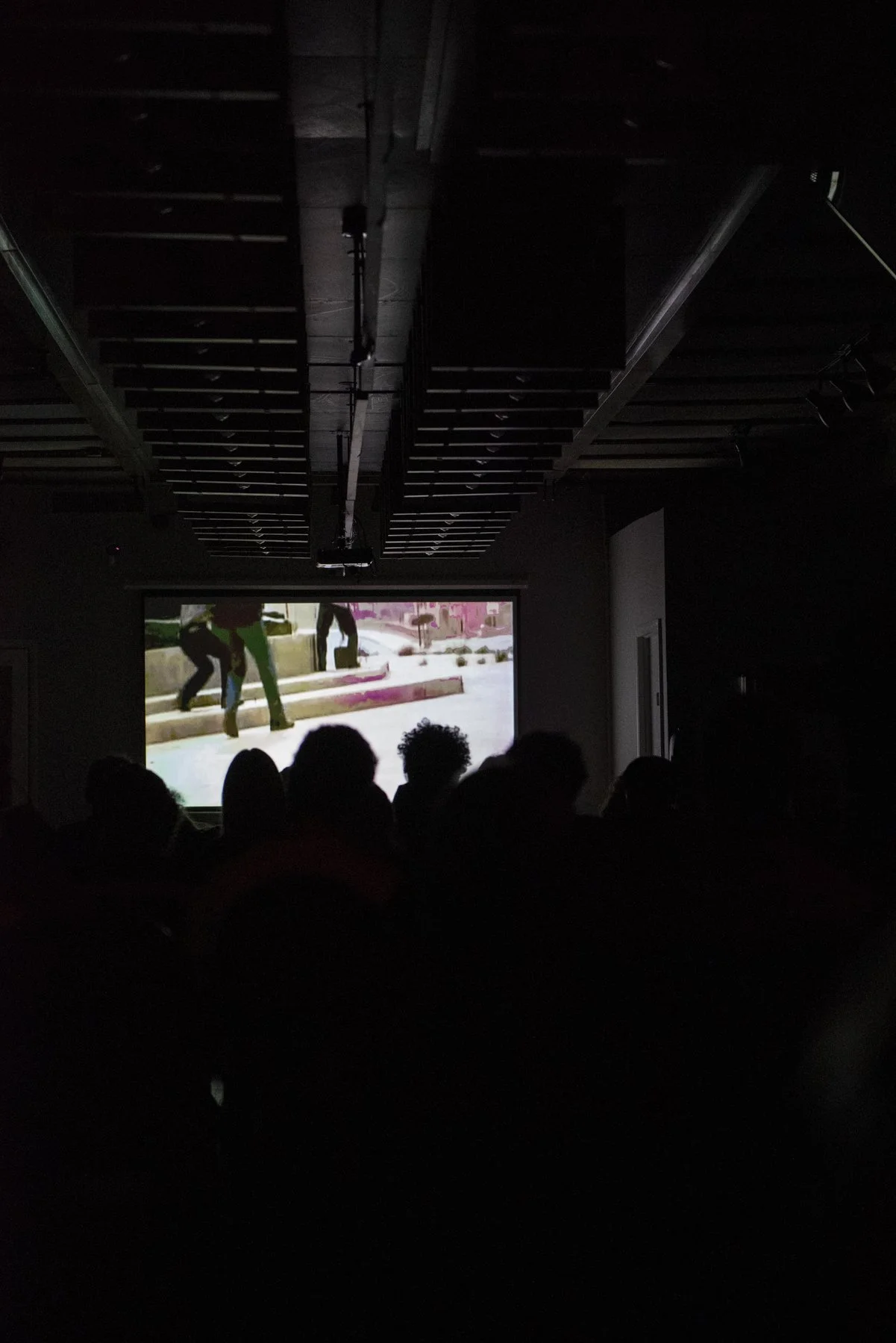 'Parallel Construction' view of screening. Dark room with silhouettes of people watching a movie.