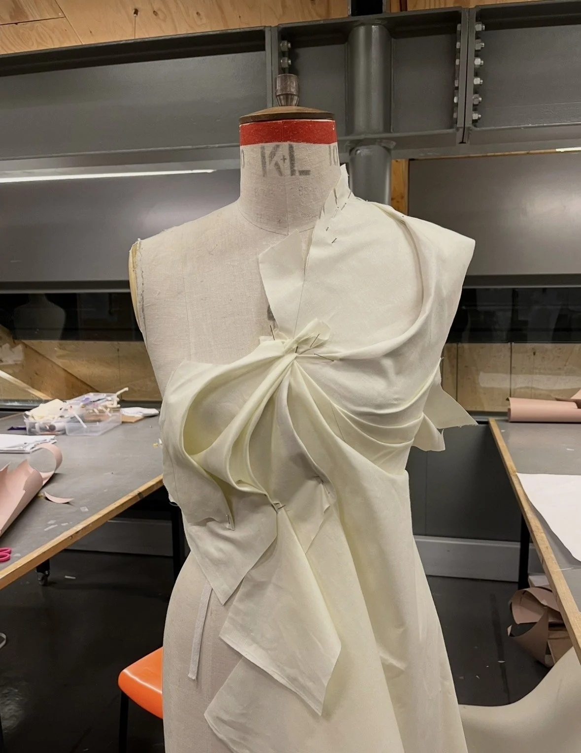 A dress form in a workshop with fabric draped around it, partially sewn for a dress or gown.