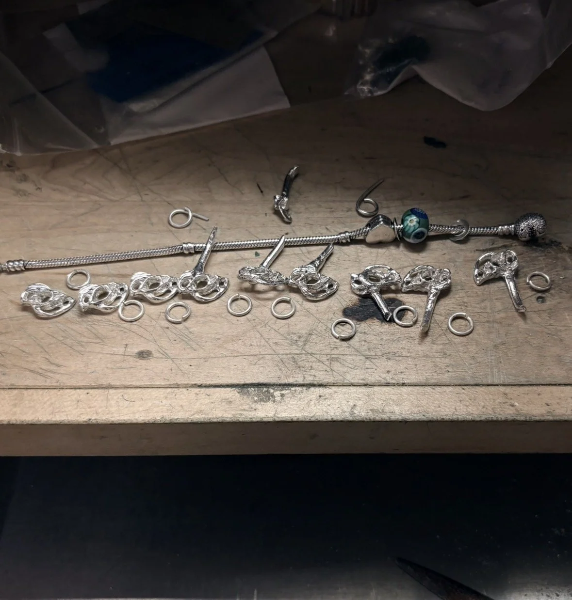 Assorted jewelry pieces, including charms and beads, scattered on a wooden surface, with some tools visible nearby.