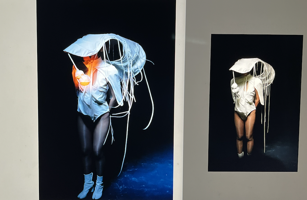 Two photographs of a woman wearing a hoodie, shorts, and thigh-high socks, holding an umbrella with hanging fabric strips, set against dark backgrounds.
