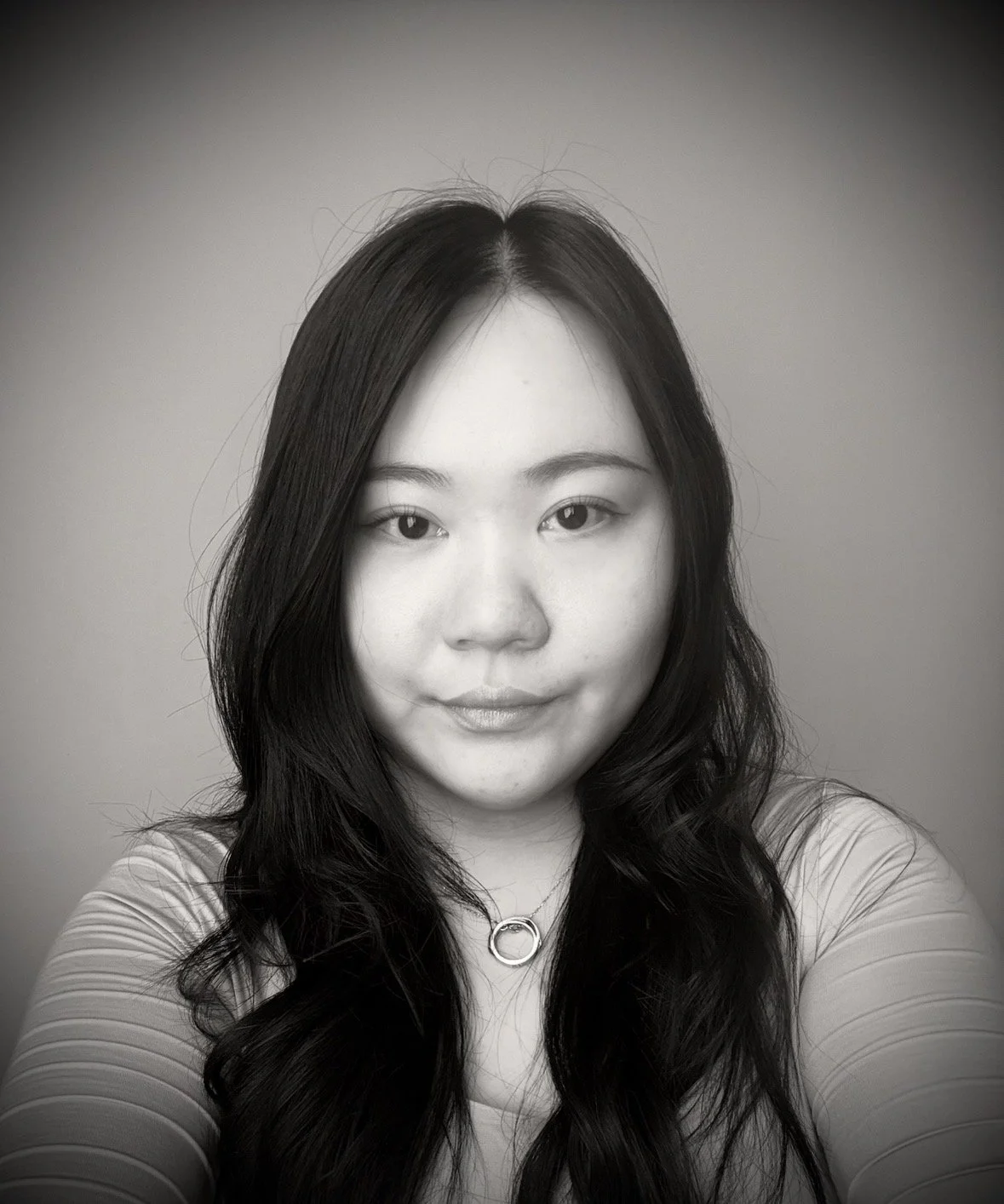 Black and white portrait of a woman with long wavy hair, wearing a round necklace, looking into the camera.