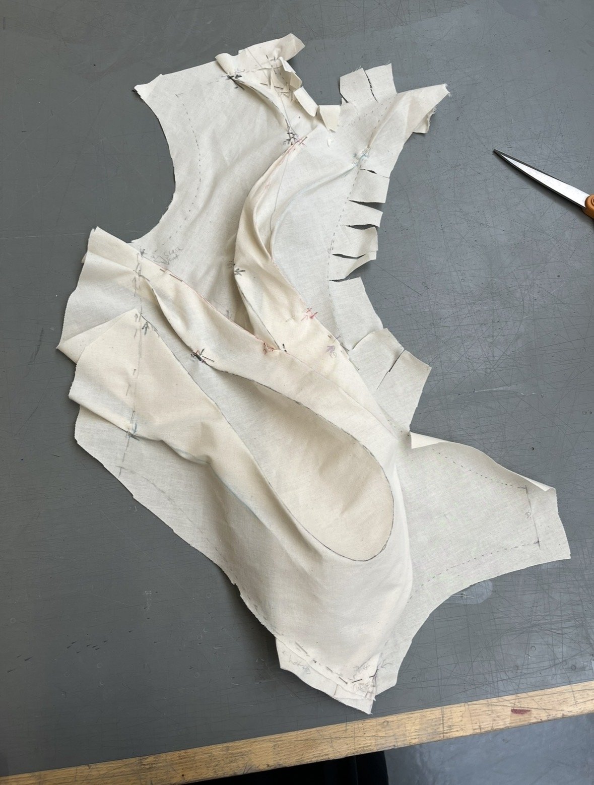 A fabric pattern with sewn lines and markings, likely a sewing or tailoring project, on a flat surface with a pair of scissors nearby.