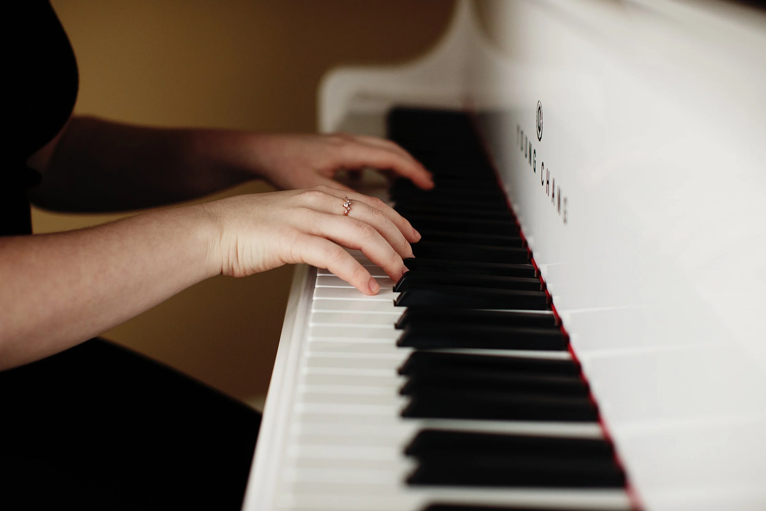 Close-up of hands playing piano keys, one wearing a ring, with white and black keys visible.