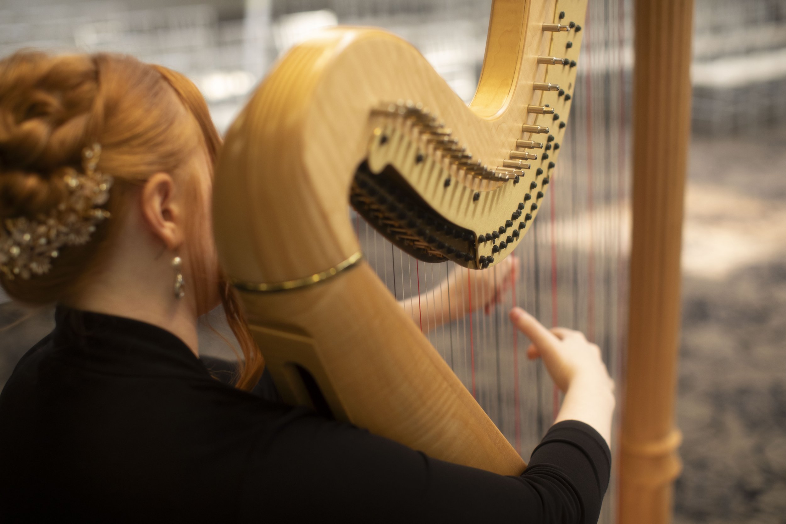 A woman with red hair adorned with flowers is playing a harp.