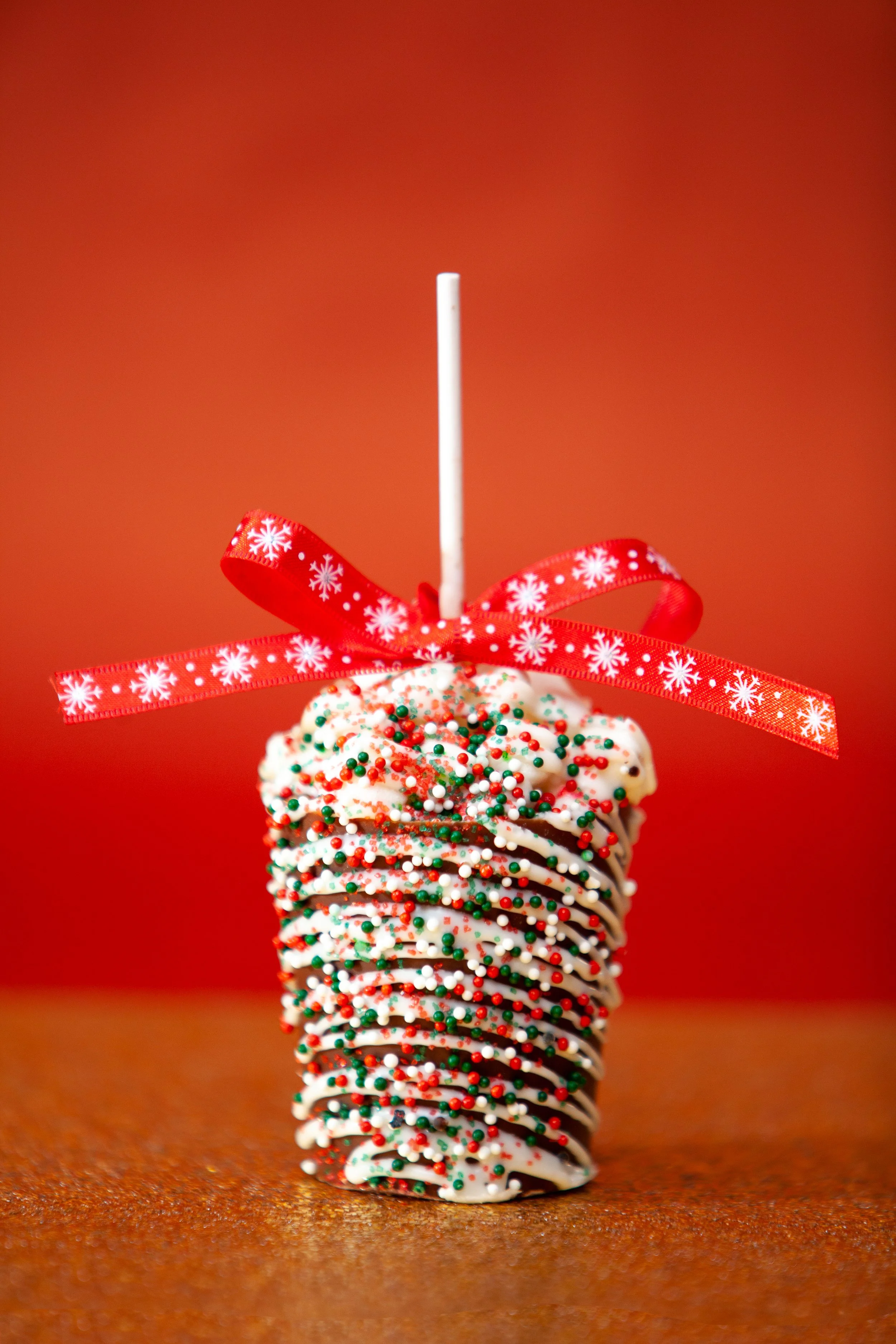 A decorated Christmas dessert resembling a snowflake, topped with colorful sprinkles and a red ribbon, with a white straw on a red background.