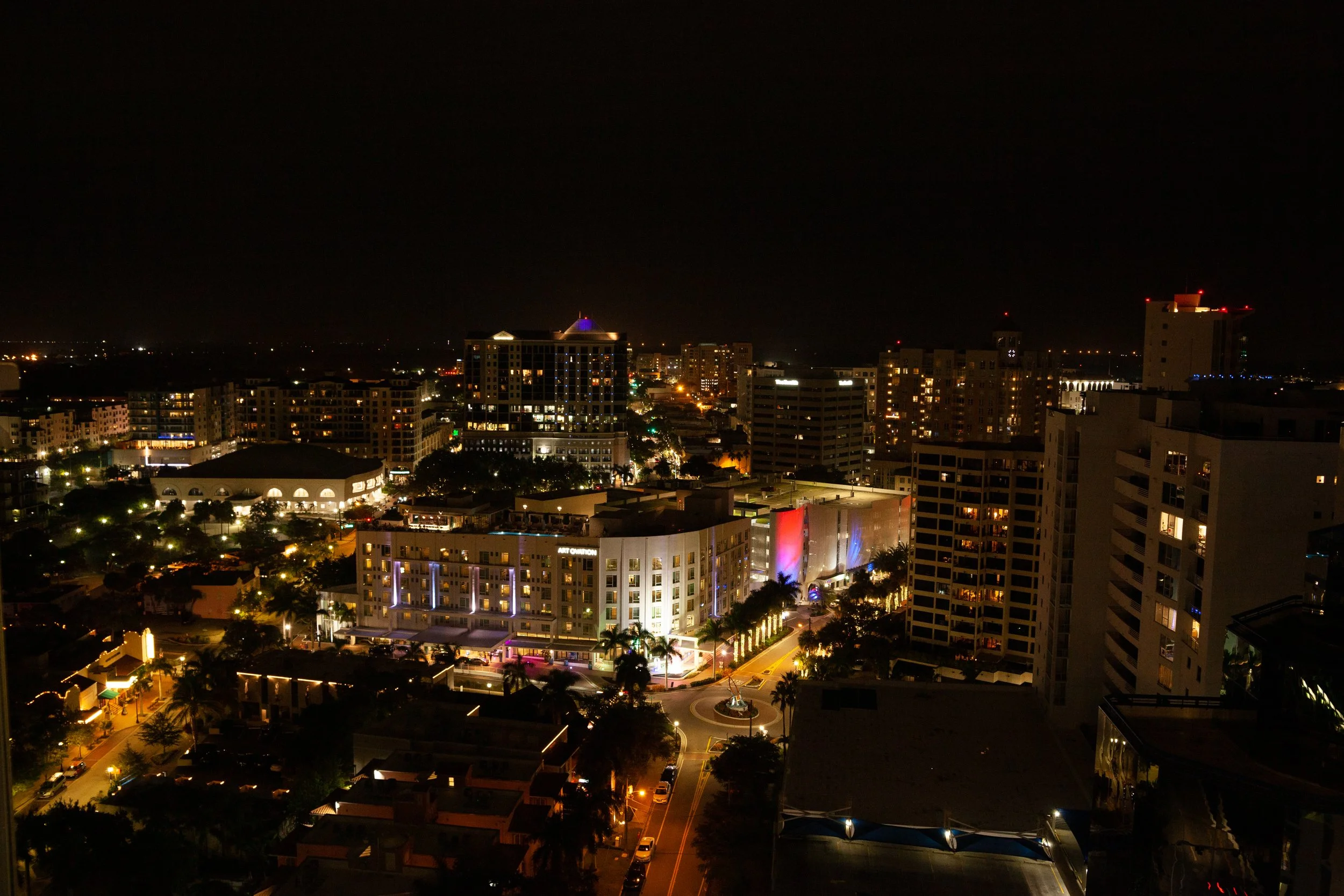 Nighttime cityscape with illuminated buildings, streets, and palm trees in Miami.